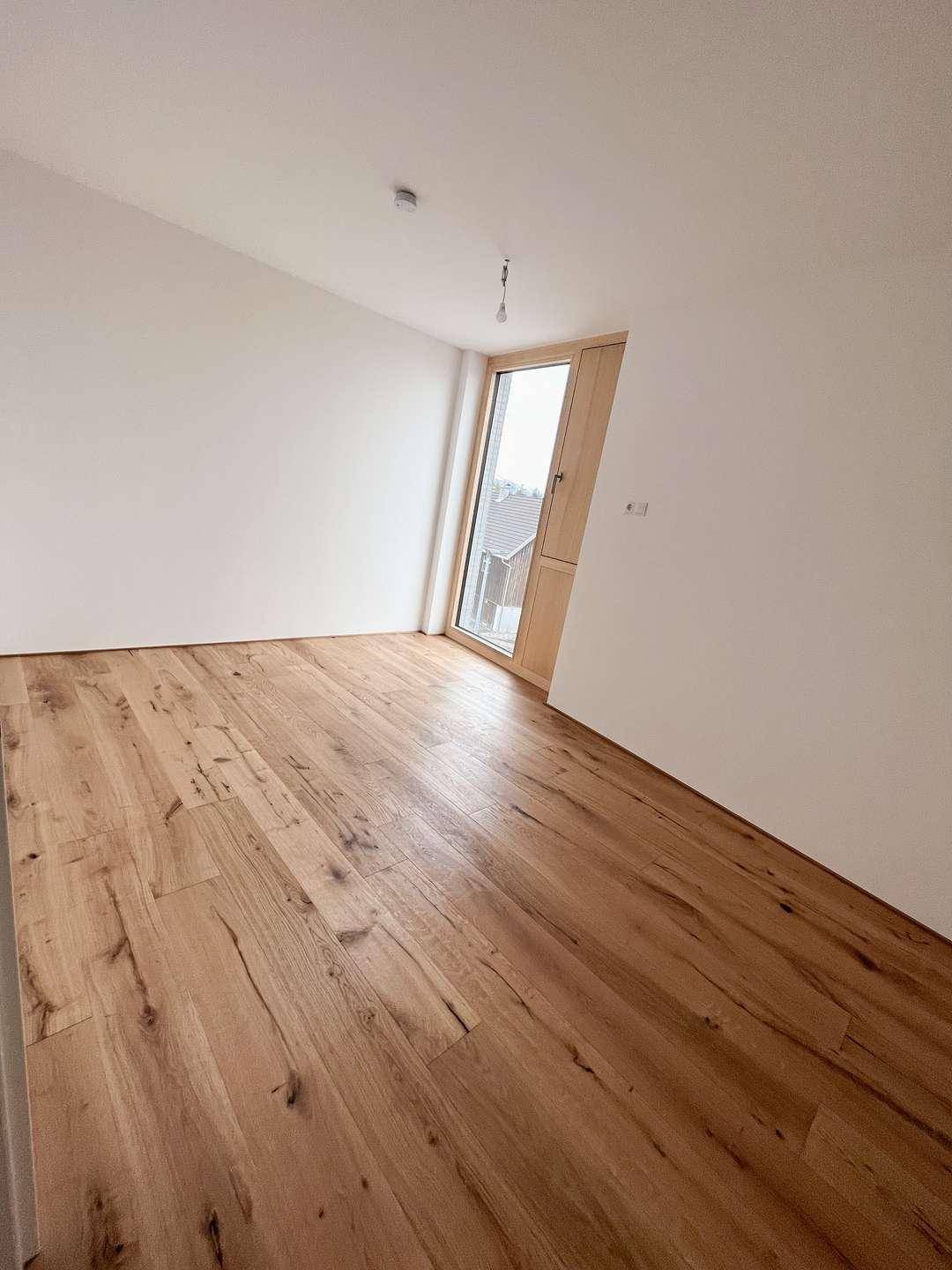 Geräumiges Schlafzimmer mit hellem Holzboden und einem modernen Fenster, das den Raum erhellt.