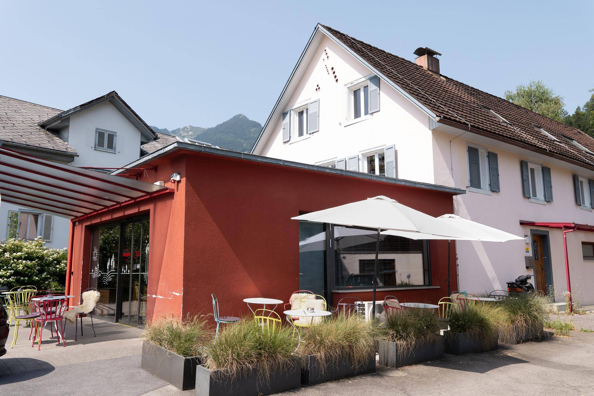 Gebäude mit roter Ladenfront und einem einladenden Außensitzbereich unter einem Sonnenschirm.