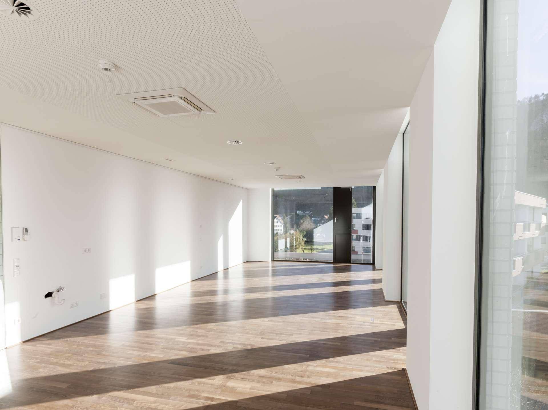 Langer, heller Büroraum mit Holzboden, großen Fenstern und viel Sonnenlicht, ideal für flexible Nutzung.