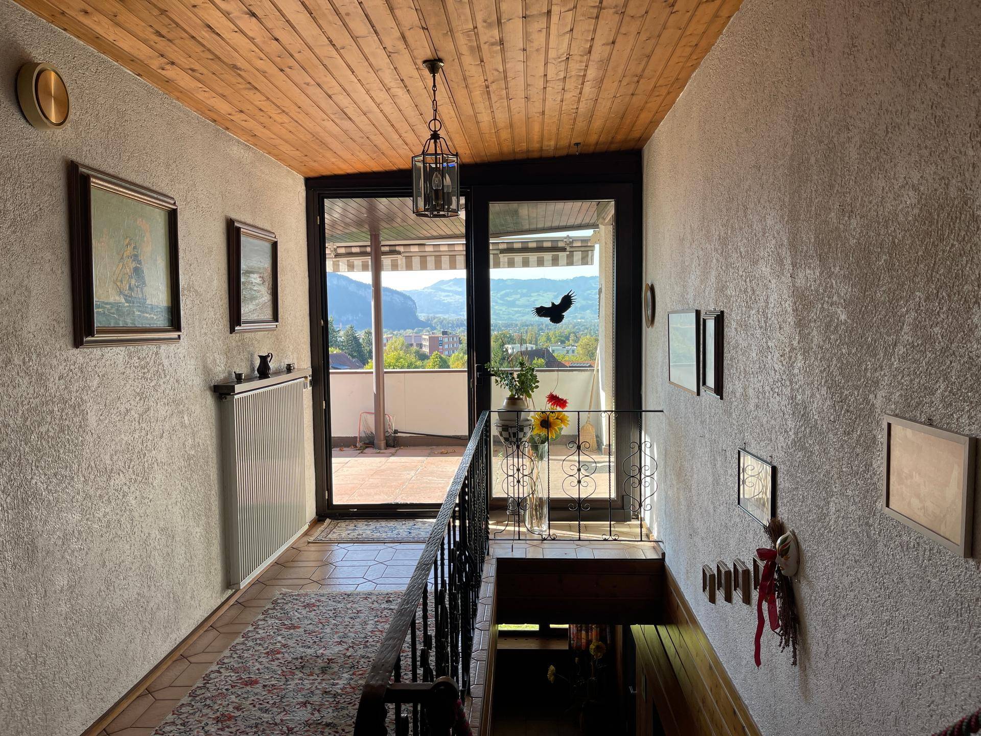 Heller Flur mit Holzdecke und Fliesenboden, der zu einem Balkon mit Bergblick führt.