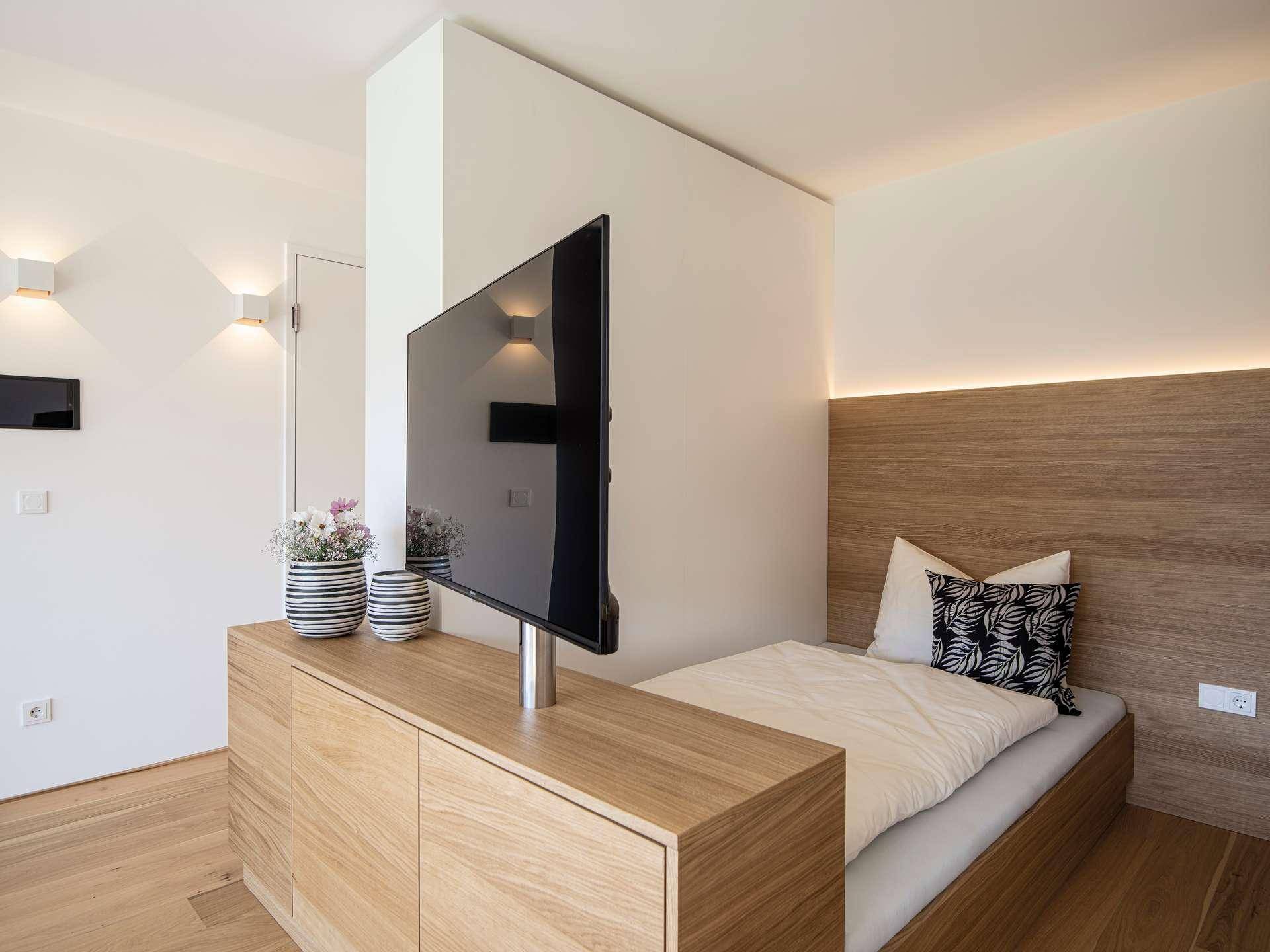 Schlafzimmer mit Holzboden und einem TV auf einem eleganten Holzschrank am Fußende des Bettes.