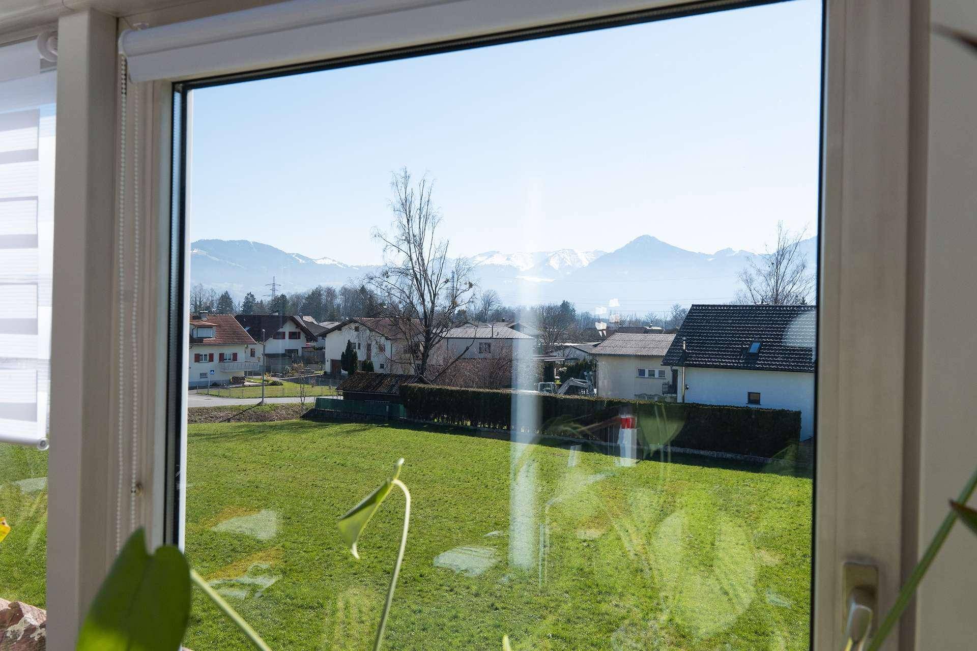 Weitblick aus dem Fenster über grüne Wiesen und schneebedeckte Berge.