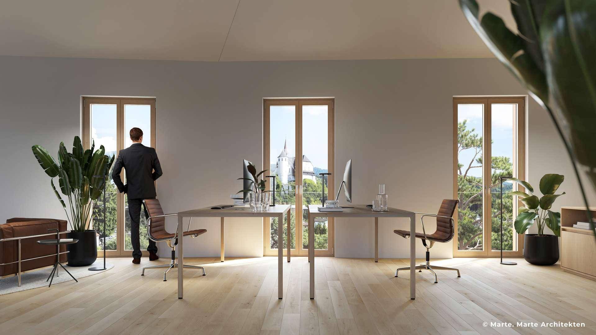 Helles, modernes Büro mit mehreren Arbeitsplätzen, großen Fenstern und Blick auf eine historische Kirche.