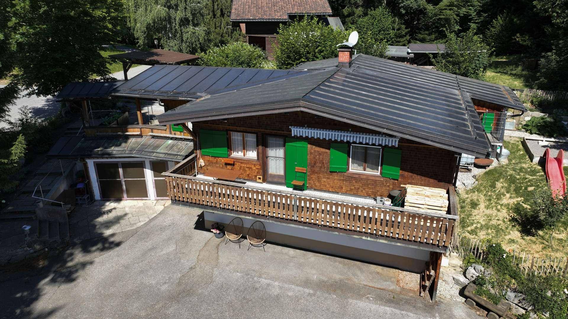 Luftaufnahme des Holzchalets mit Solaranlage auf dem Dach, Balkon und umgebender Natur.