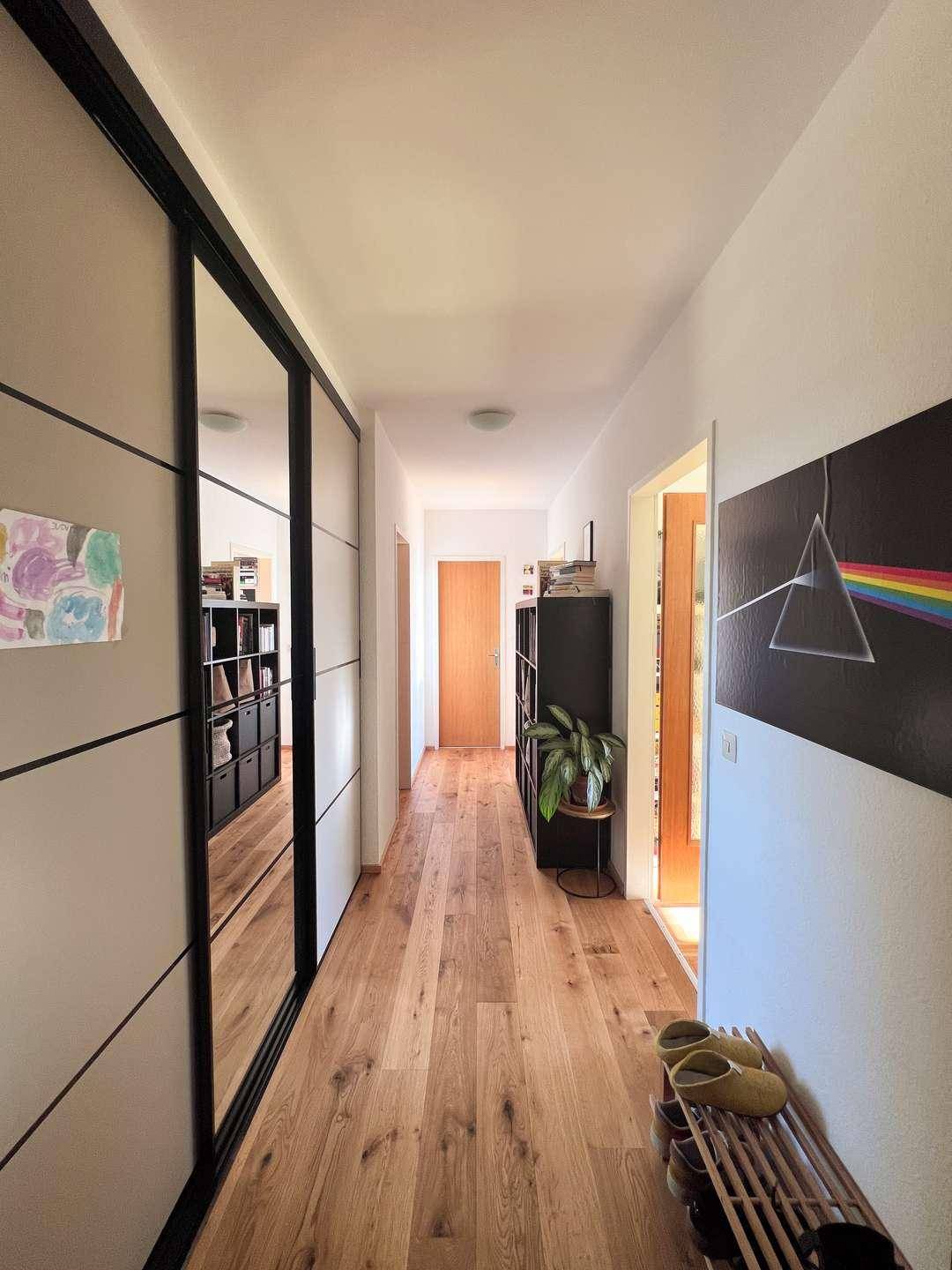 Langer Flur mit Holzboden, Spiegelschränken und dekorativer Kunst an der Wand.
