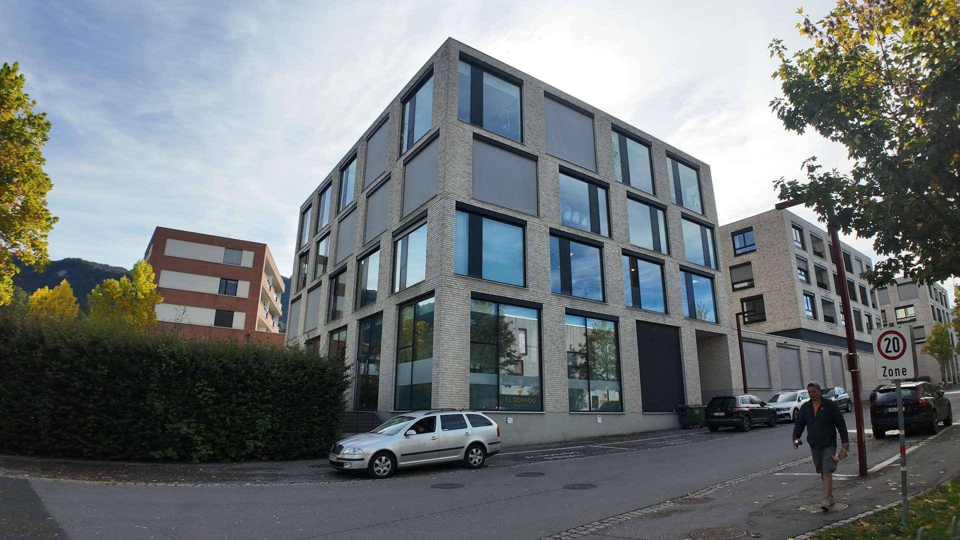 Modernes Bürogebäude mit großen Fenstern und einer gepflegten Hecke im Vordergrund, an einer Straße gelegen.