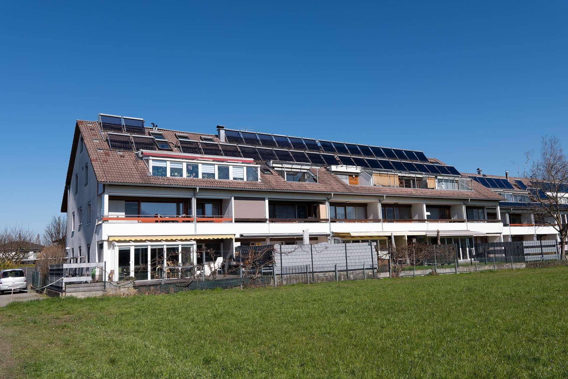 Mehrfamilienhaus mit Solaranlagen auf dem Dach und grüner Umgebung.