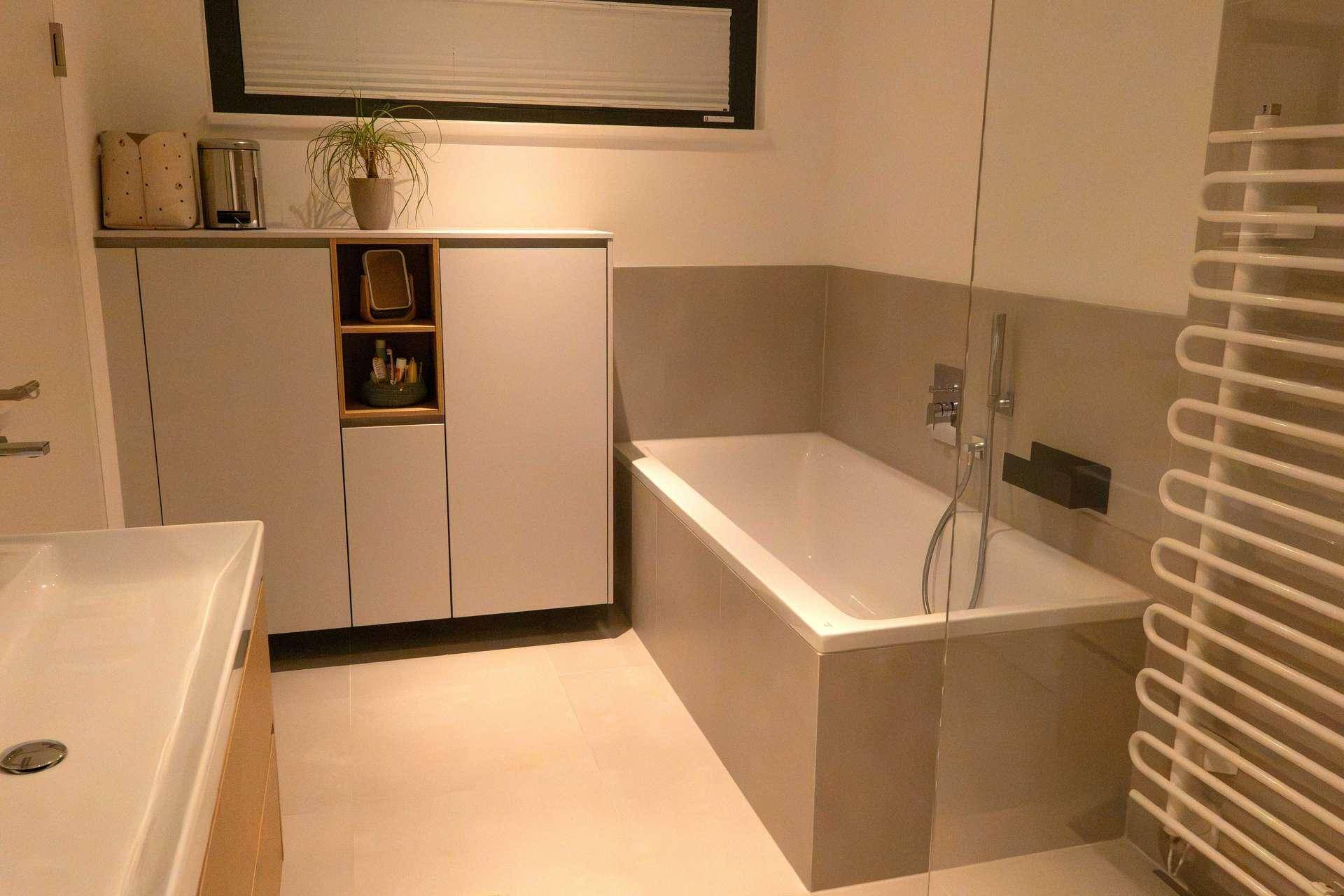 Helles Badezimmer mit Badewanne, praktischen Schränken und Handtuchheizkörper.