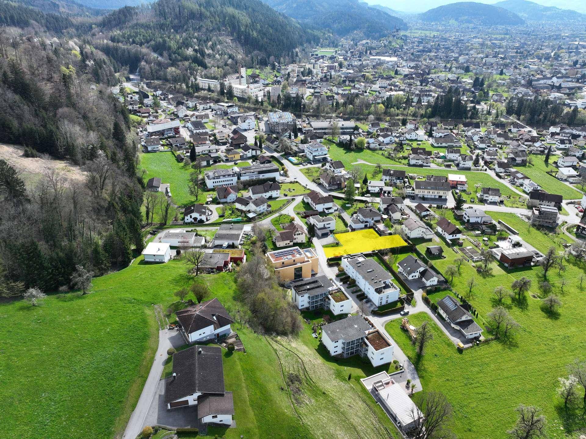 Panoramablick aus der Luft auf eine Wohnsiedlung, umgeben von grünen Hügeln und Bergen.