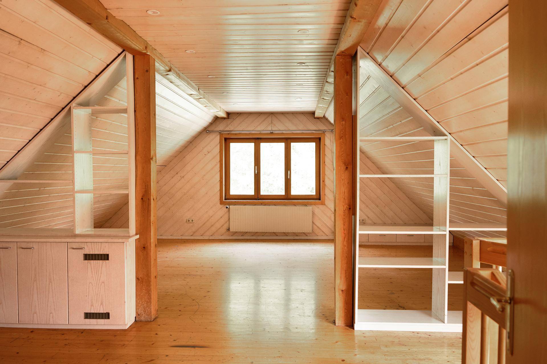 Heller Dachbodenraum mit schrägen Holzdecken, Holzboden und praktischen Einbauregalen.