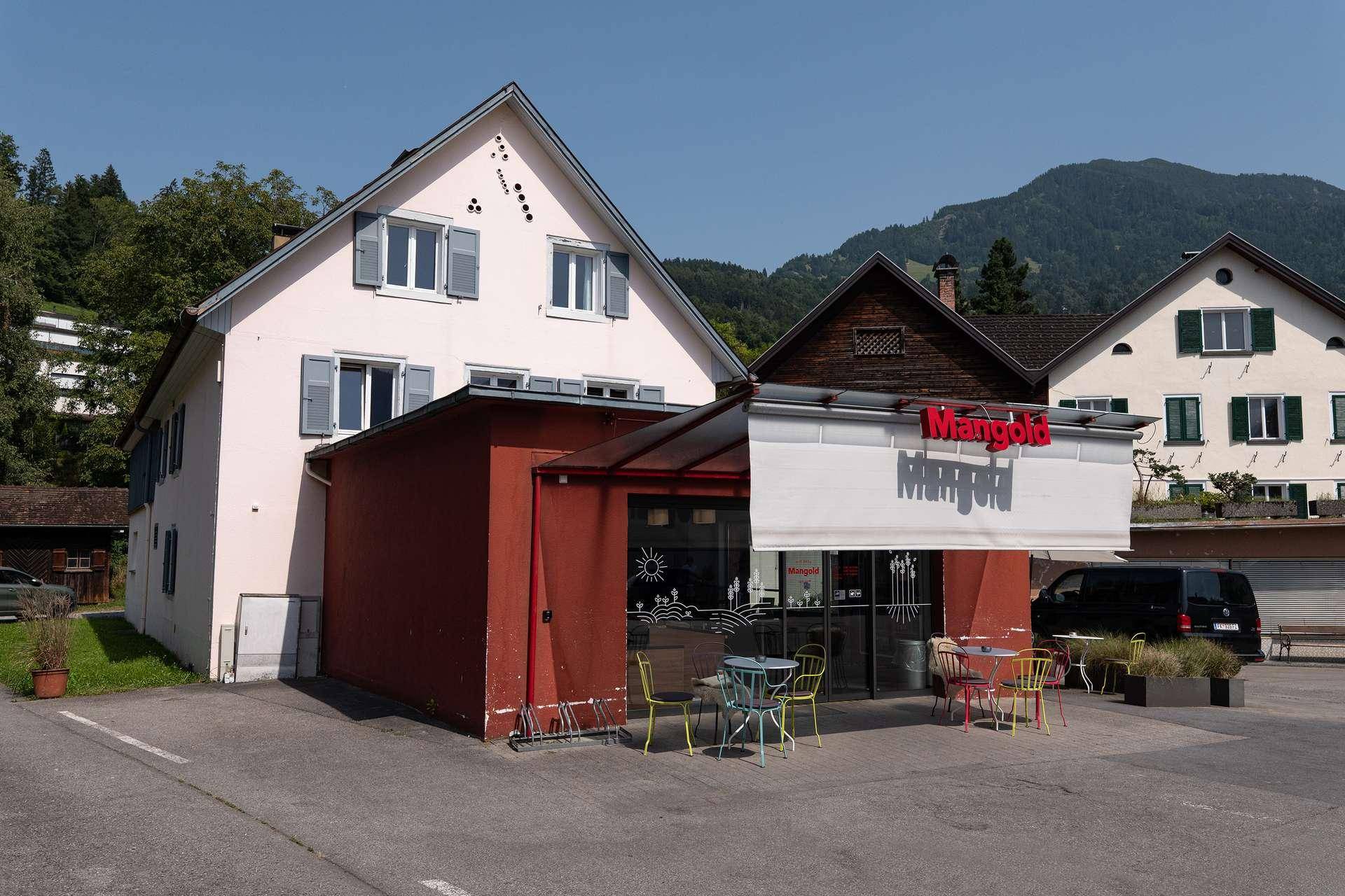 Detailansicht des Gebäudes mit dem Café im Erdgeschoss und der Fassade mit hellblauen Fensterläden.