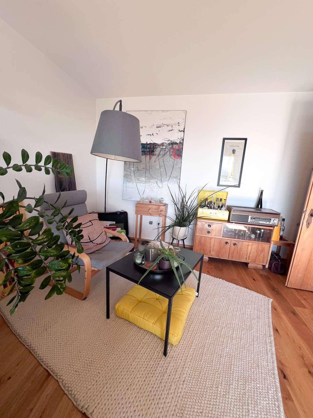 Gemütlicher Wohnbereich mit Sessel, Stehlampe und Holzboden, dekoriert mit Pflanzen und Kunst.