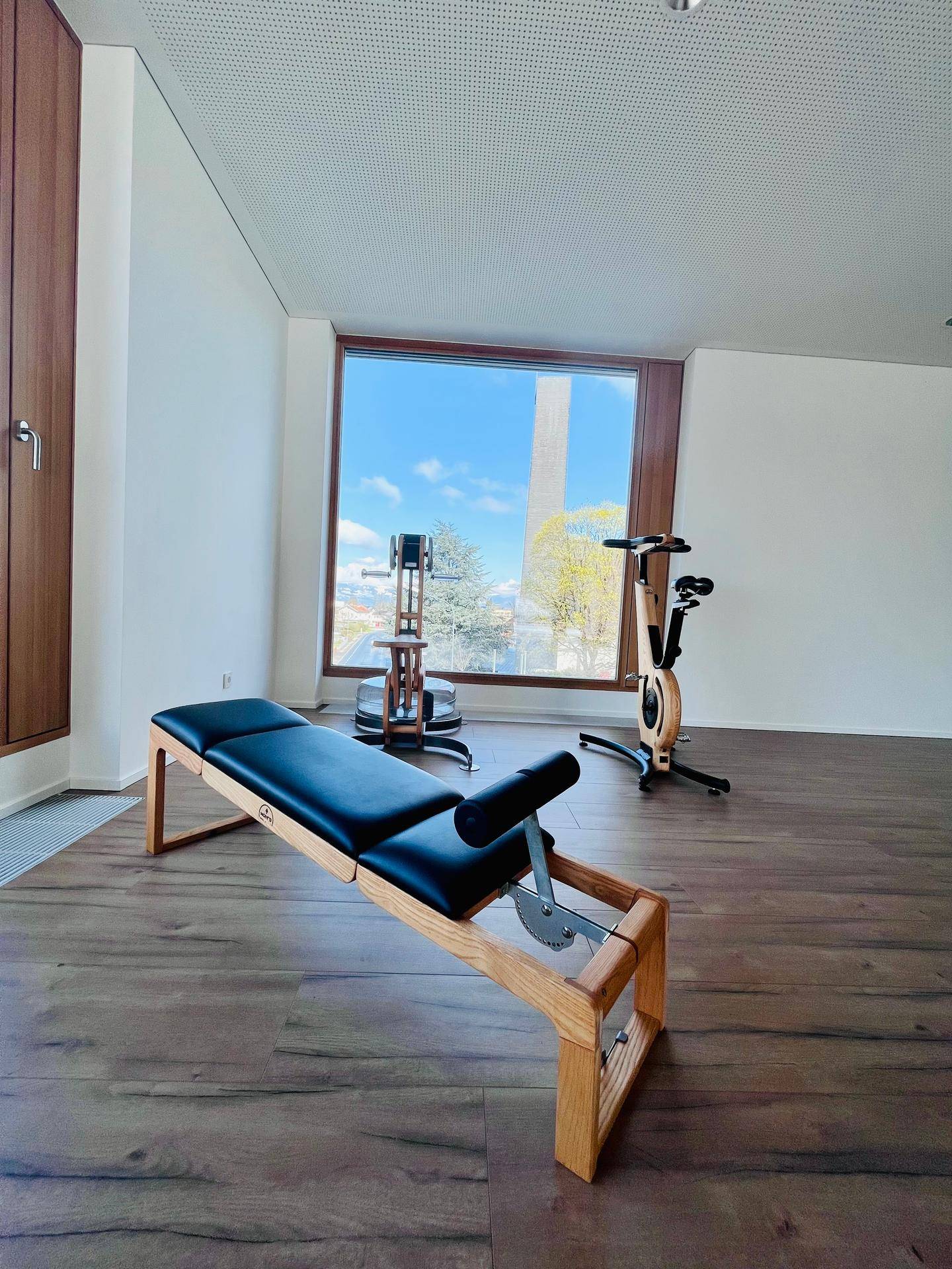 Trainingsbereich mit modernen Holzgeräten und großem Fenster, das viel Tageslicht hereinlässt und eine schöne Aussicht bietet.