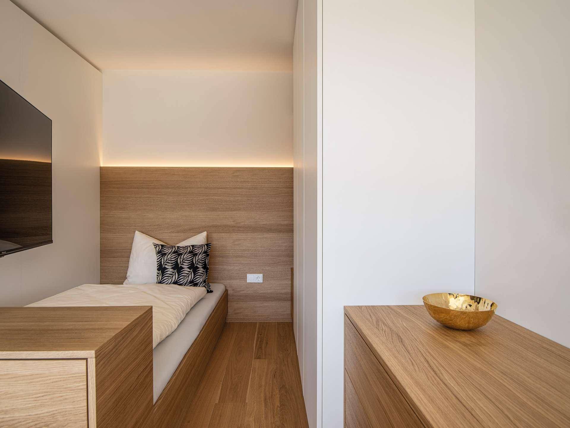 Kompaktes Schlafzimmer mit Holzbett und integrierten Möbeln, hell und modern gestaltet.