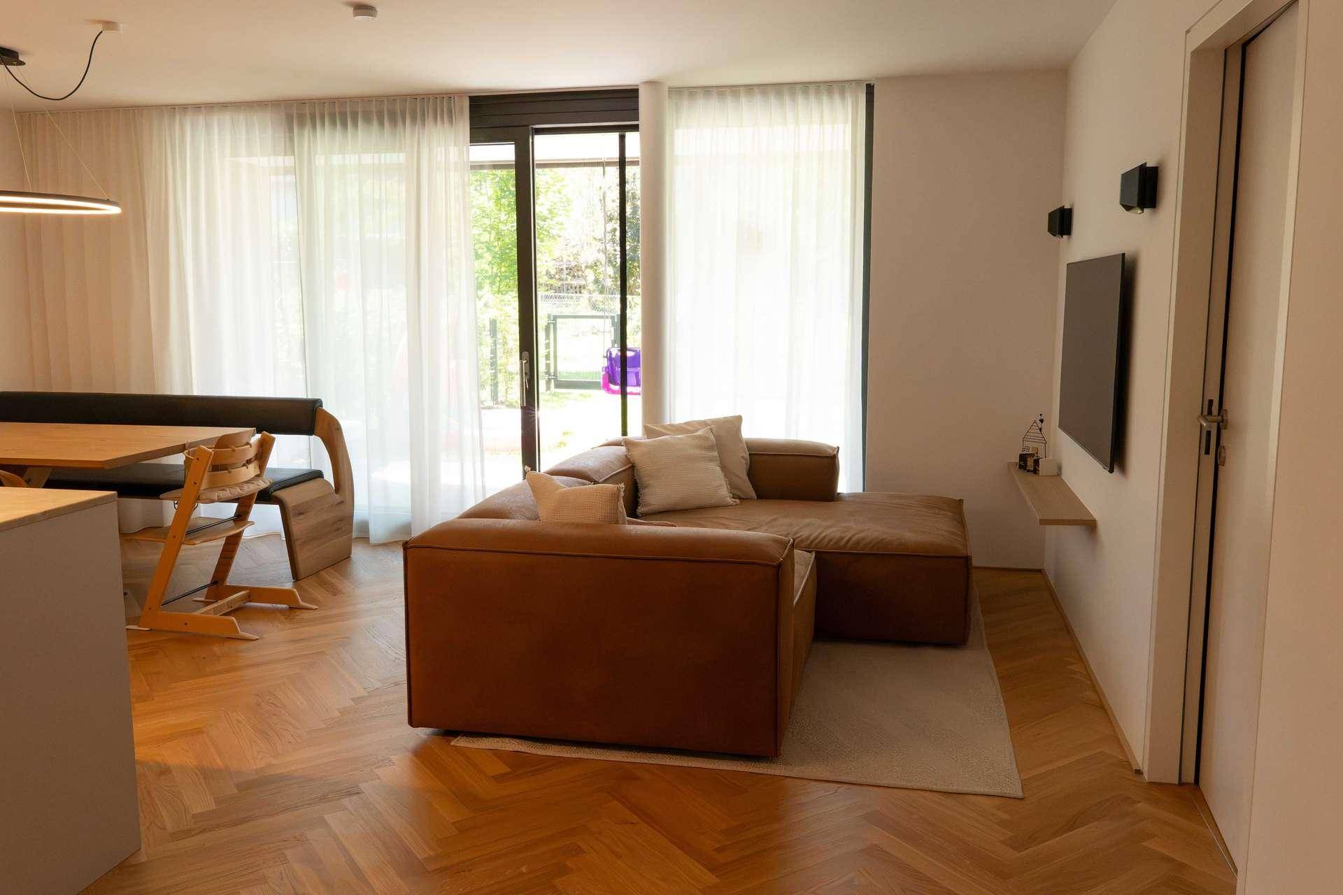 Offener Wohn-Essbereich mit bequemer Couch, Holzboden und Zugang zum Garten.