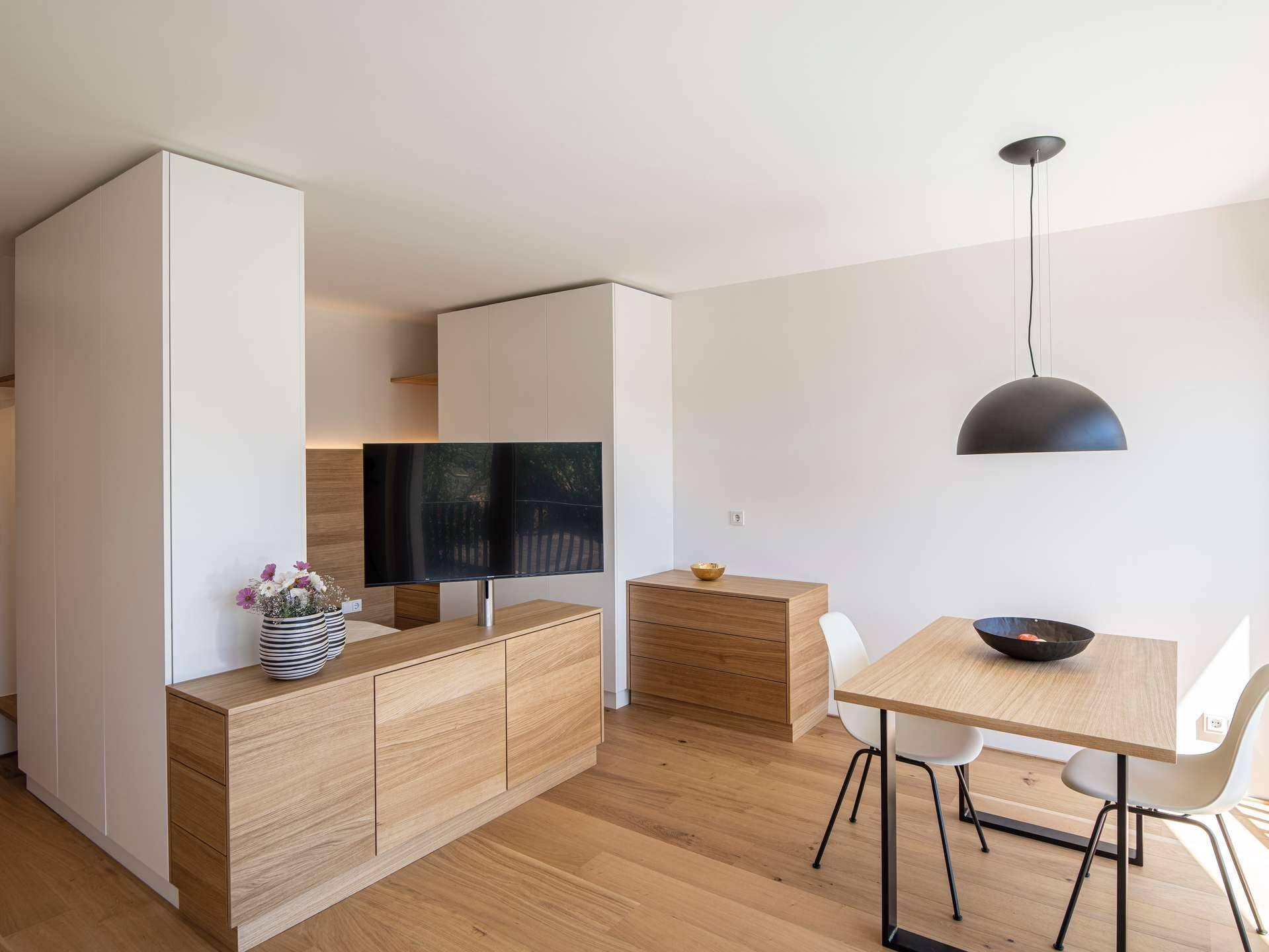 Offener Wohn-Essbereich mit Holzboden, modernem Esstisch und einem TV-Möbel aus Holz.