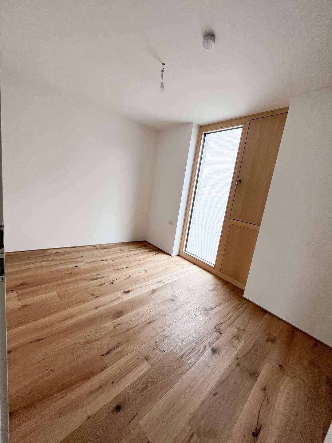 Helles Schlafzimmer mit Holzdielenboden und einem schrägen Fenster, das viel Licht hereinlässt.