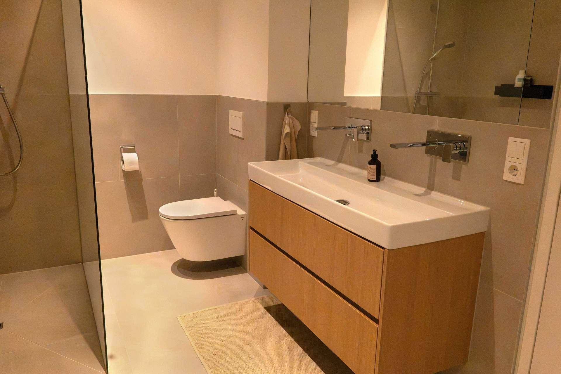 Modernes Badezimmer mit Doppelwaschbecken, Wand-WC und großen Fliesen.