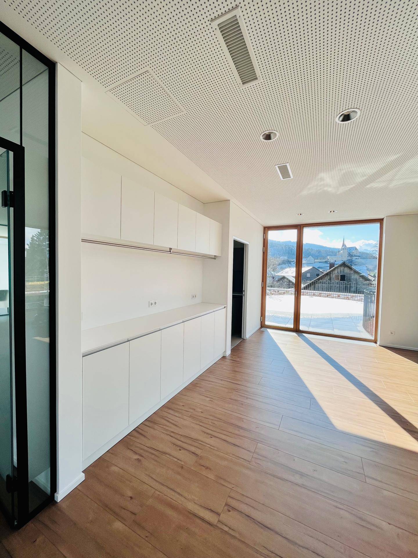 Moderne Teeküche mit weißen Schränken und großem Fenster, bietet einen malerischen Blick auf die verschneite Landschaft.