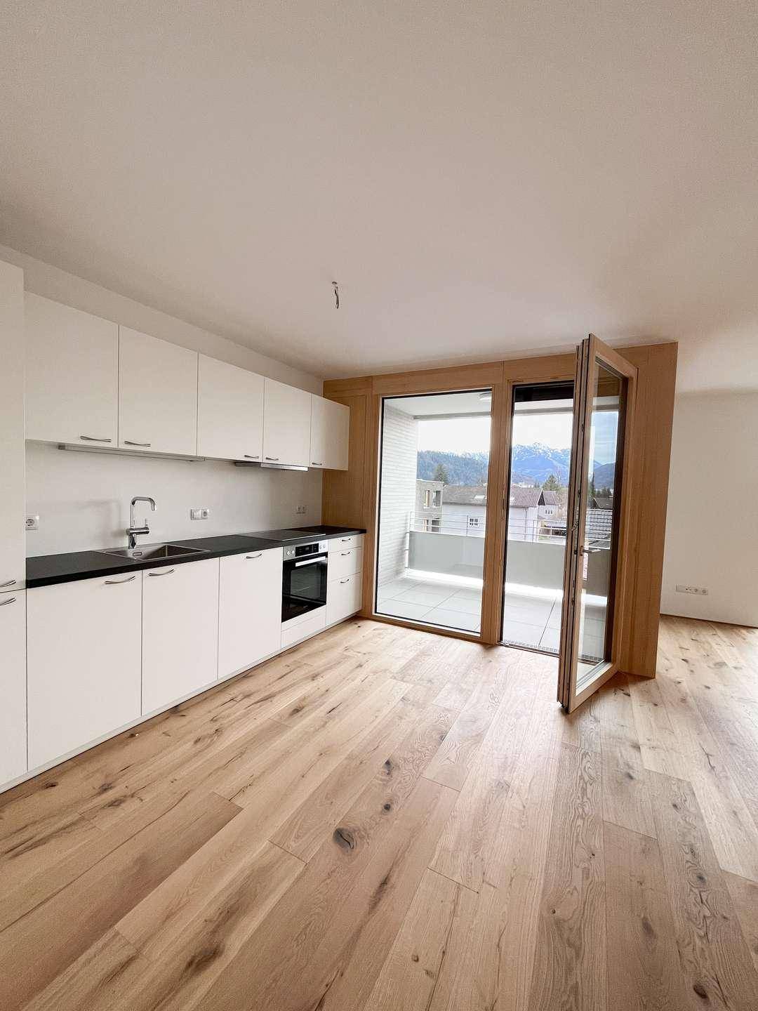 Moderne Einbauküche mit weißen Schränken, dunkler Arbeitsplatte und Zugang zum Balkon mit Bergblick.