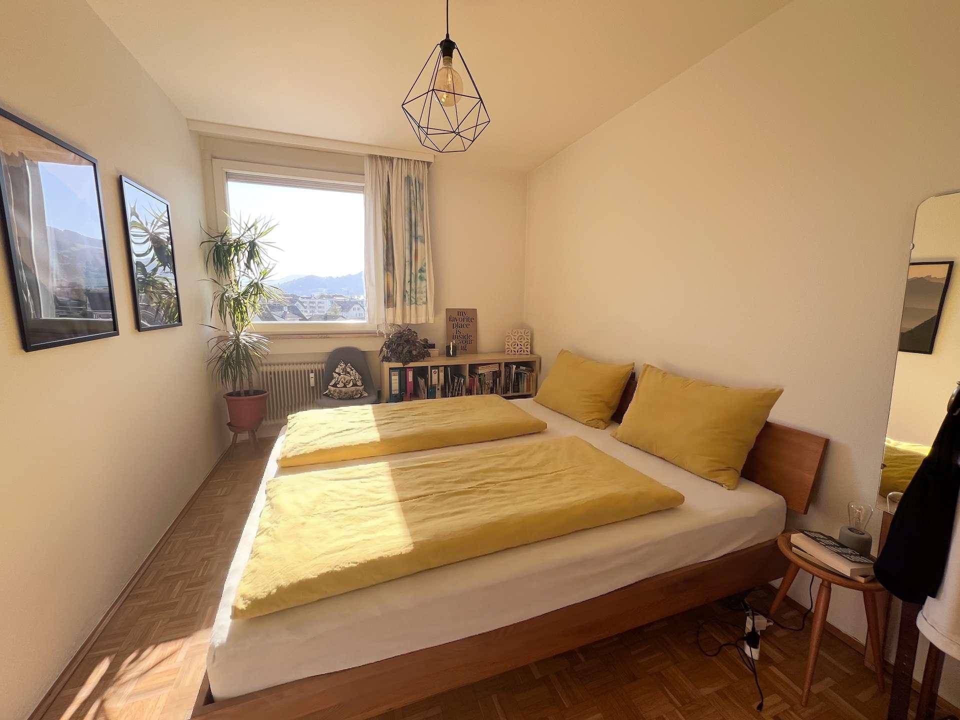 Helles Schlafzimmer mit Doppelbett, Holzboden und Fenster mit Blick auf die Umgebung.