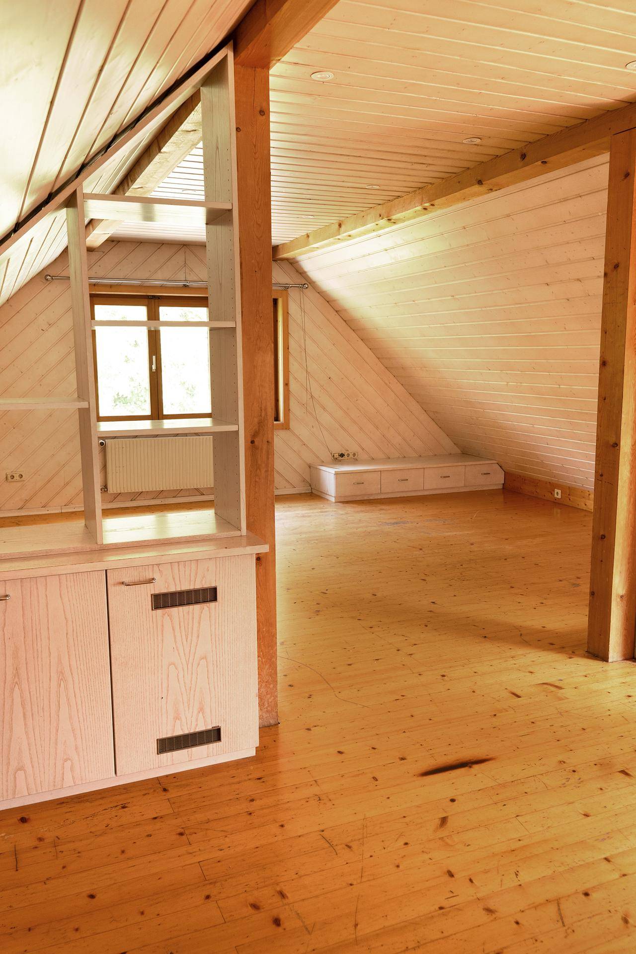 Geräumiger Dachboden mit Holzboden und schrägen Wänden, ausgestattet mit maßgefertigten Einbauregalen.