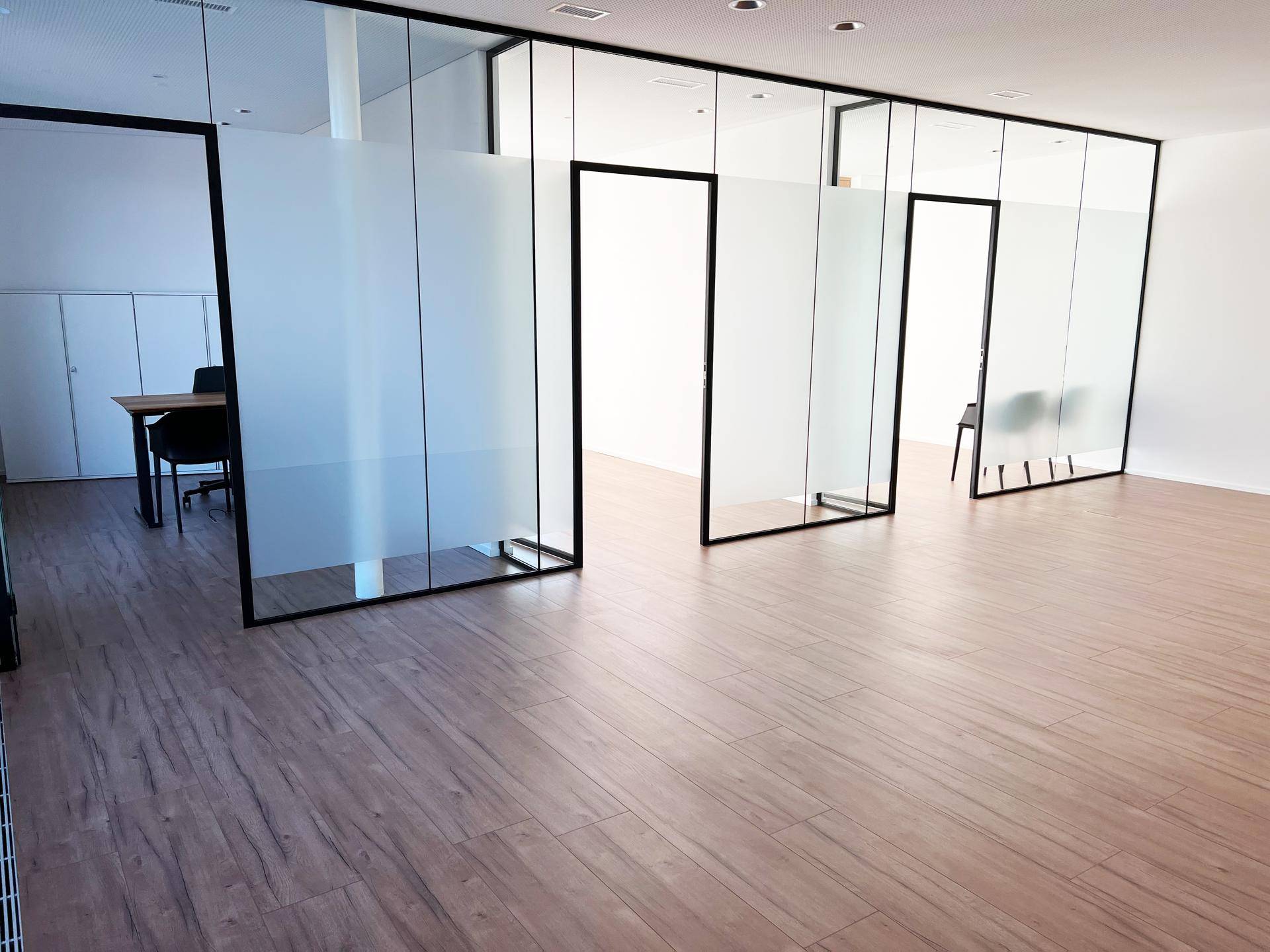Geräumiger Bürobereich mit eleganten Glaswänden und warmem Holzboden, der eine flexible Raumaufteilung ermöglicht.
