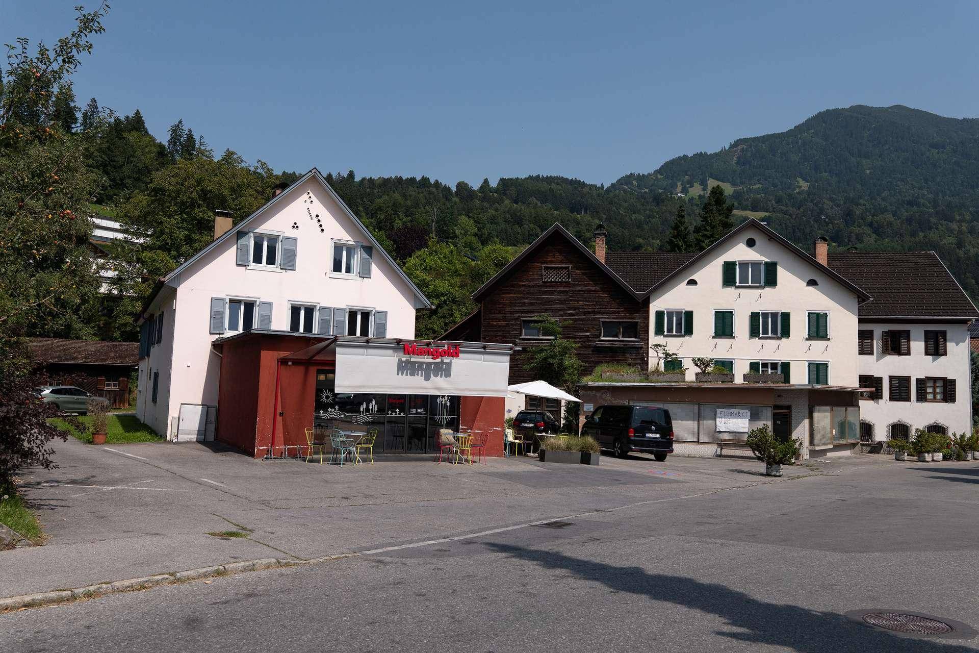 Gesamtansicht mehrerer Gebäude in einer ländlichen Umgebung, darunter ein Café und traditionelle Wohnhäuser.