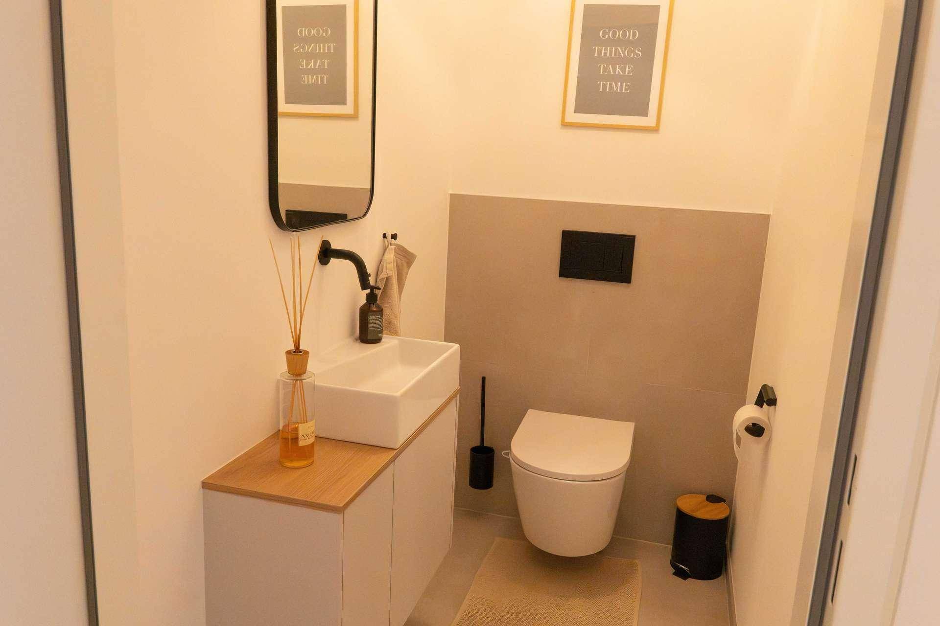 Modernes Gäste-WC mit Wand-WC, kleinem Waschbecken und Spiegel.