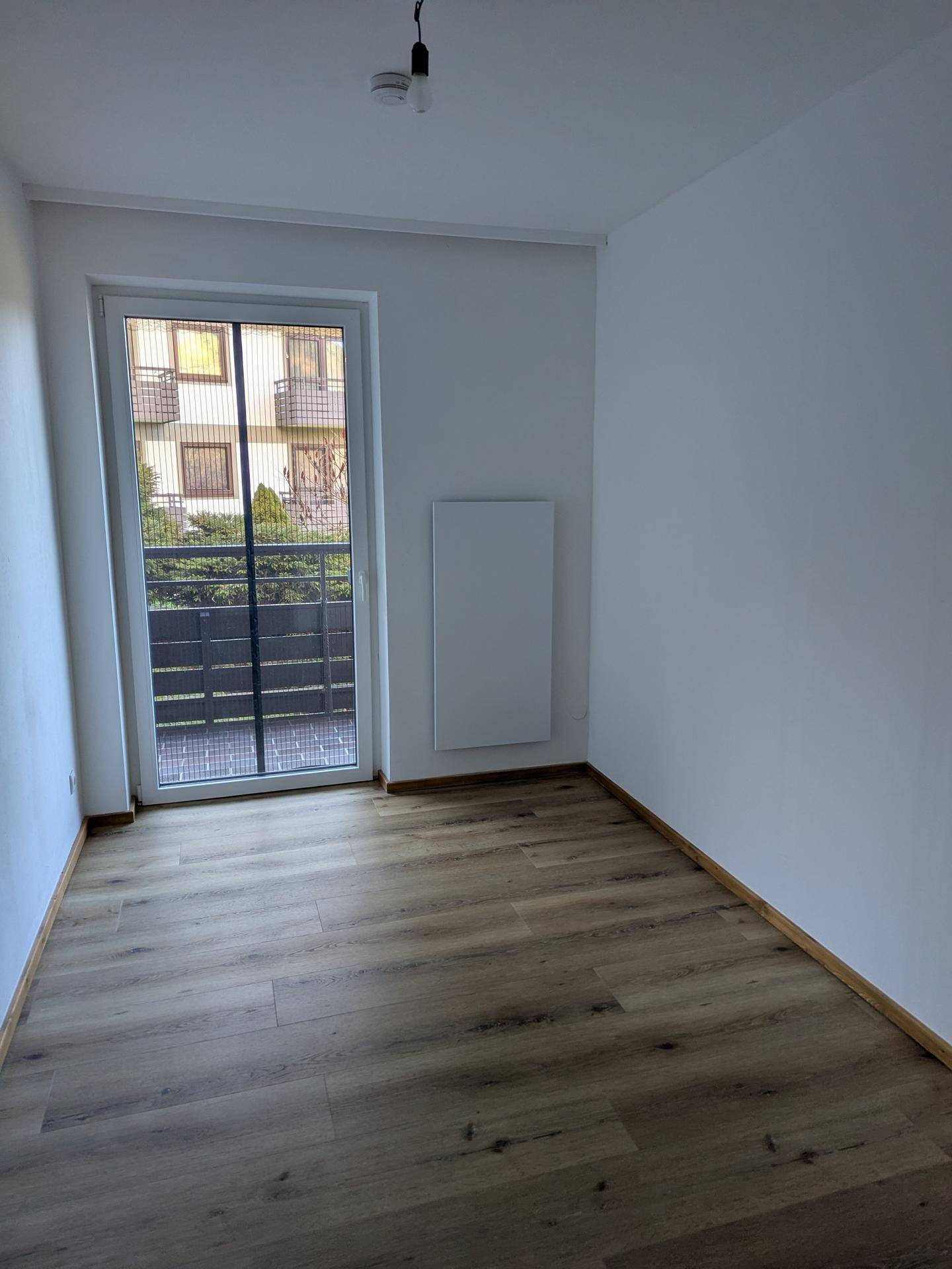 Leeres Zimmer mit Laminatboden und einer Tür, die zu einem Außenbereich führt.