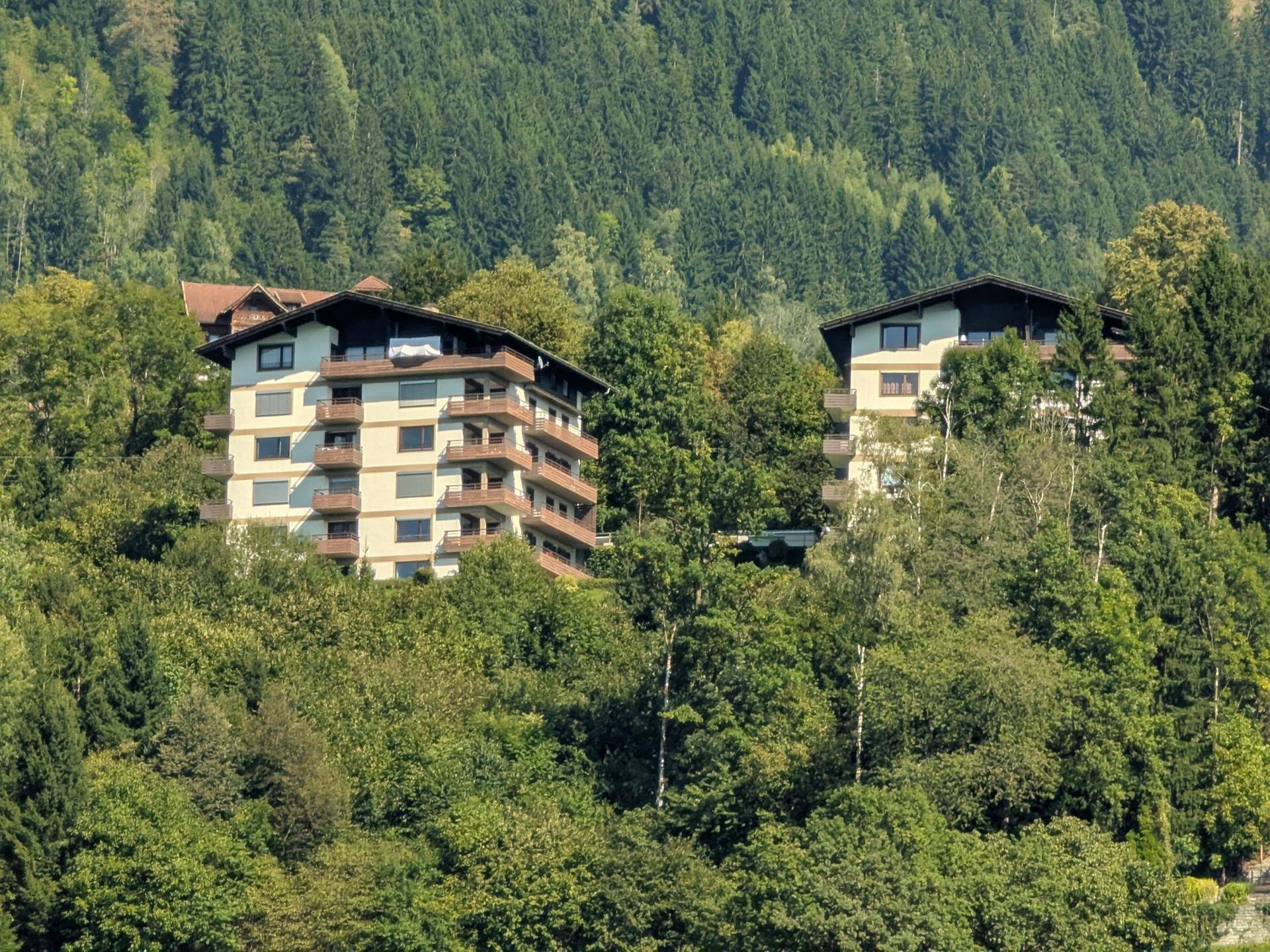 Zwei Apartmentgebäude eingebettet in eine grüne Hügellandschaft mit vielen Bäumen.