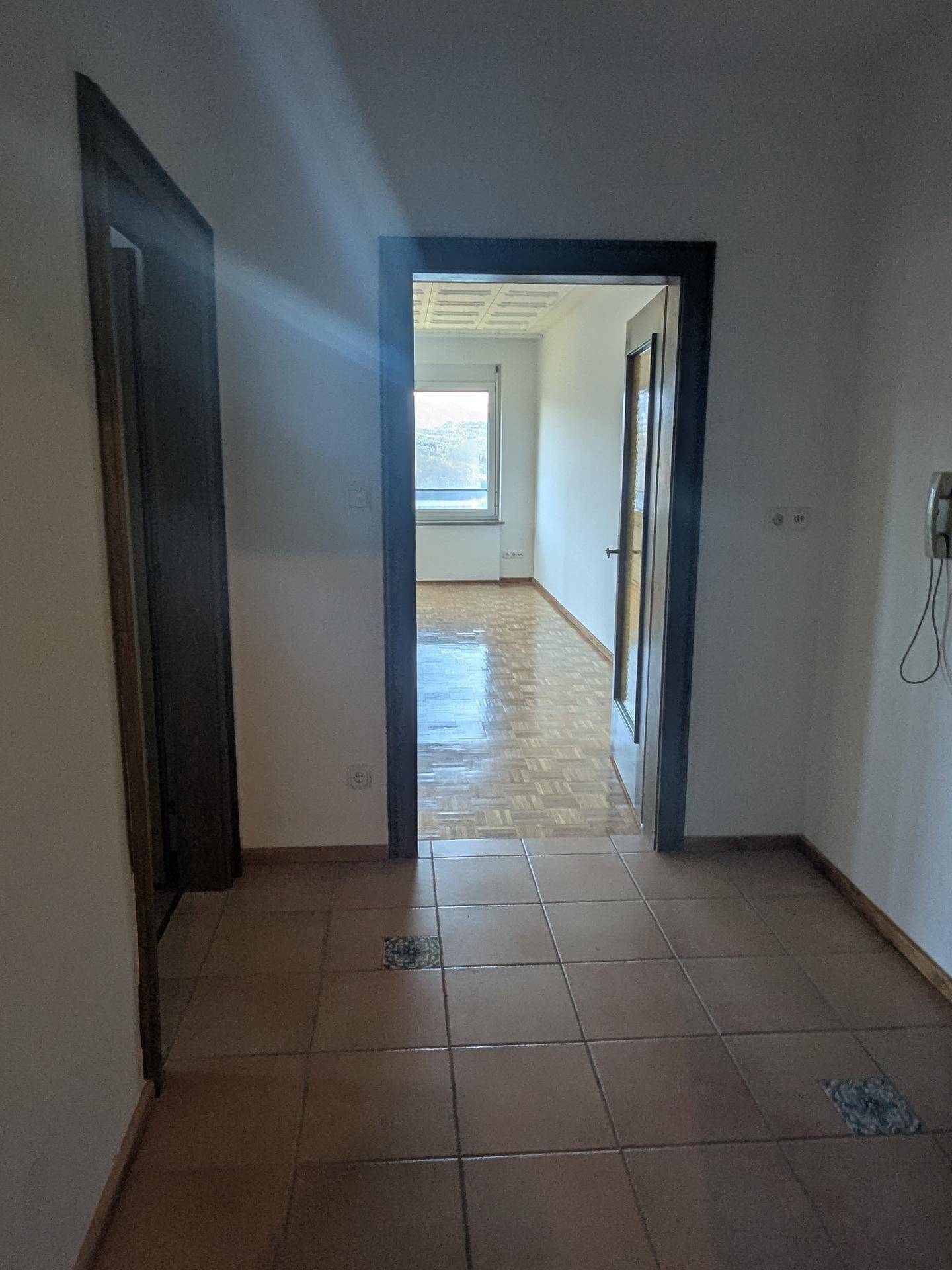 Flur mit Fliesenboden, der zu weiteren Räumen mit Parkettboden führt.