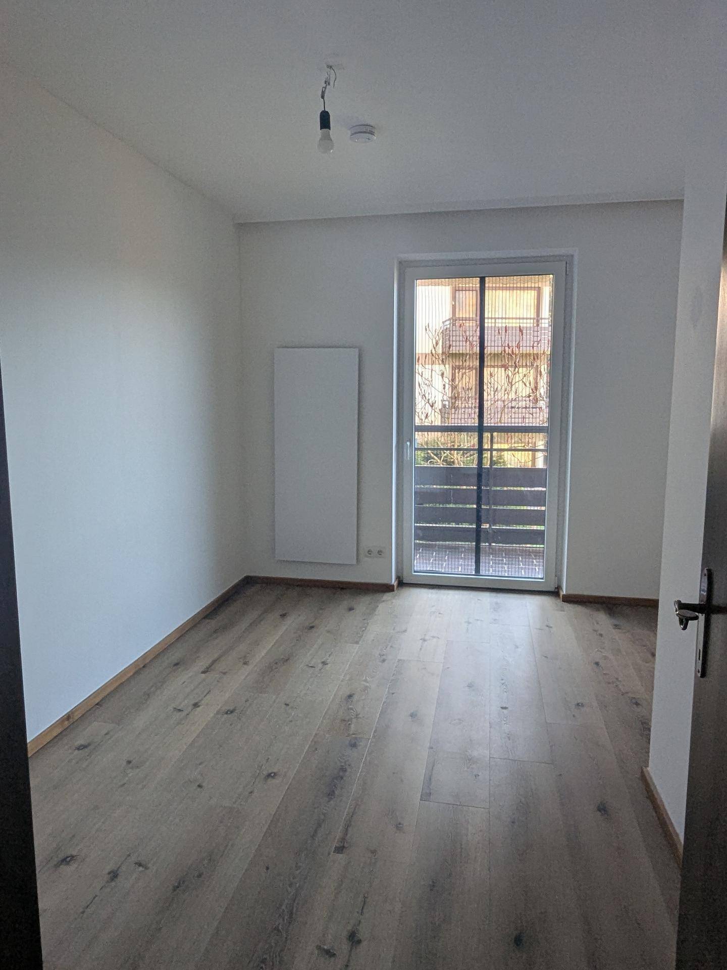 Helles Zimmer mit Laminatboden und Zugang zu einem kleinen Balkon oder französischen Balkon.