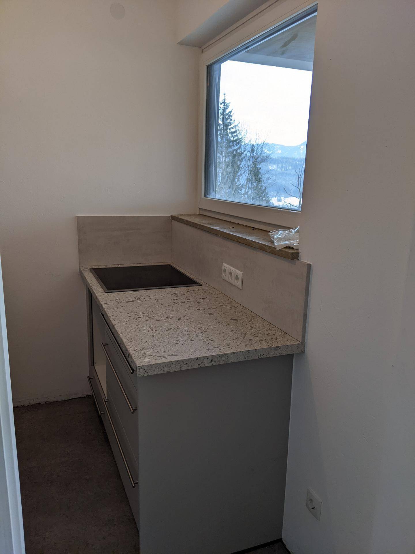 Helle Küchenzeile mit Fenster, Granitarbeitsplatte und Induktionskochfeld.