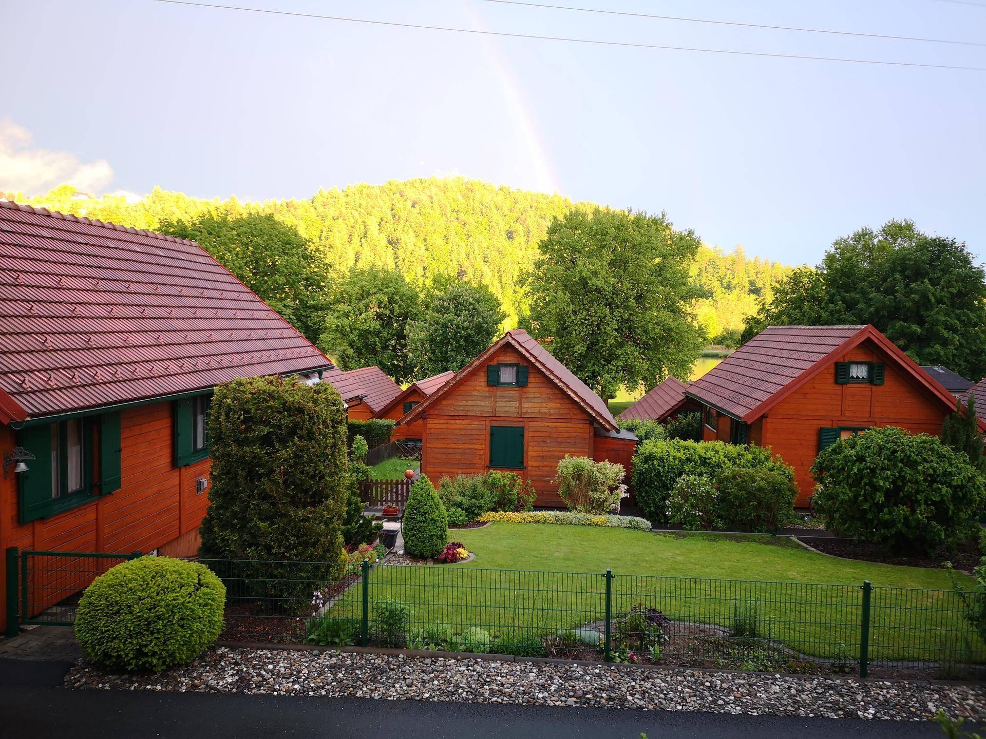 Mehrere Holzhäuser in einer grünen, hügeligen Landschaft mit gepflegten Gärten.