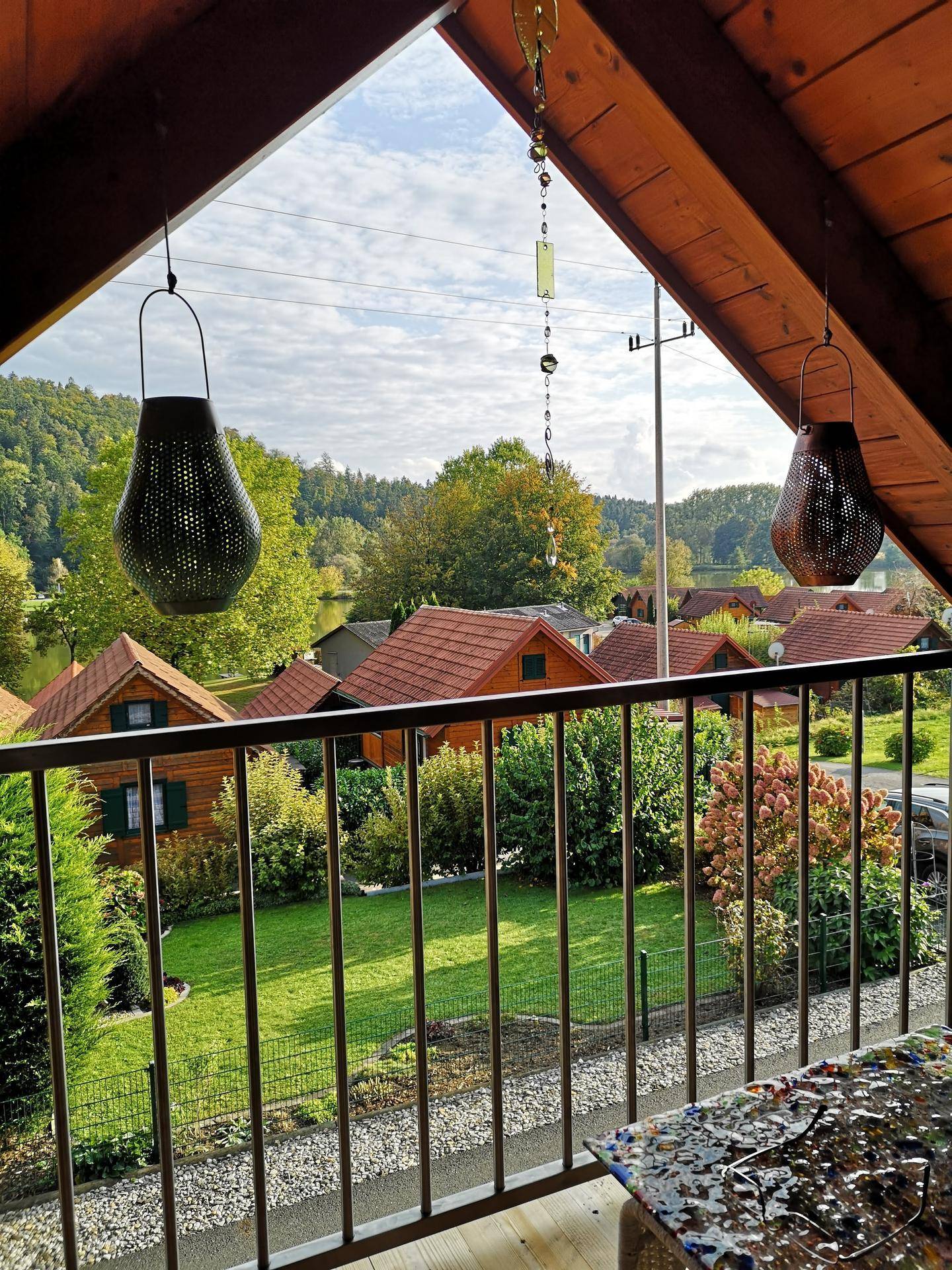 Blick vom Balkon auf die umliegenden Häuser, grüne Landschaft und einen See.