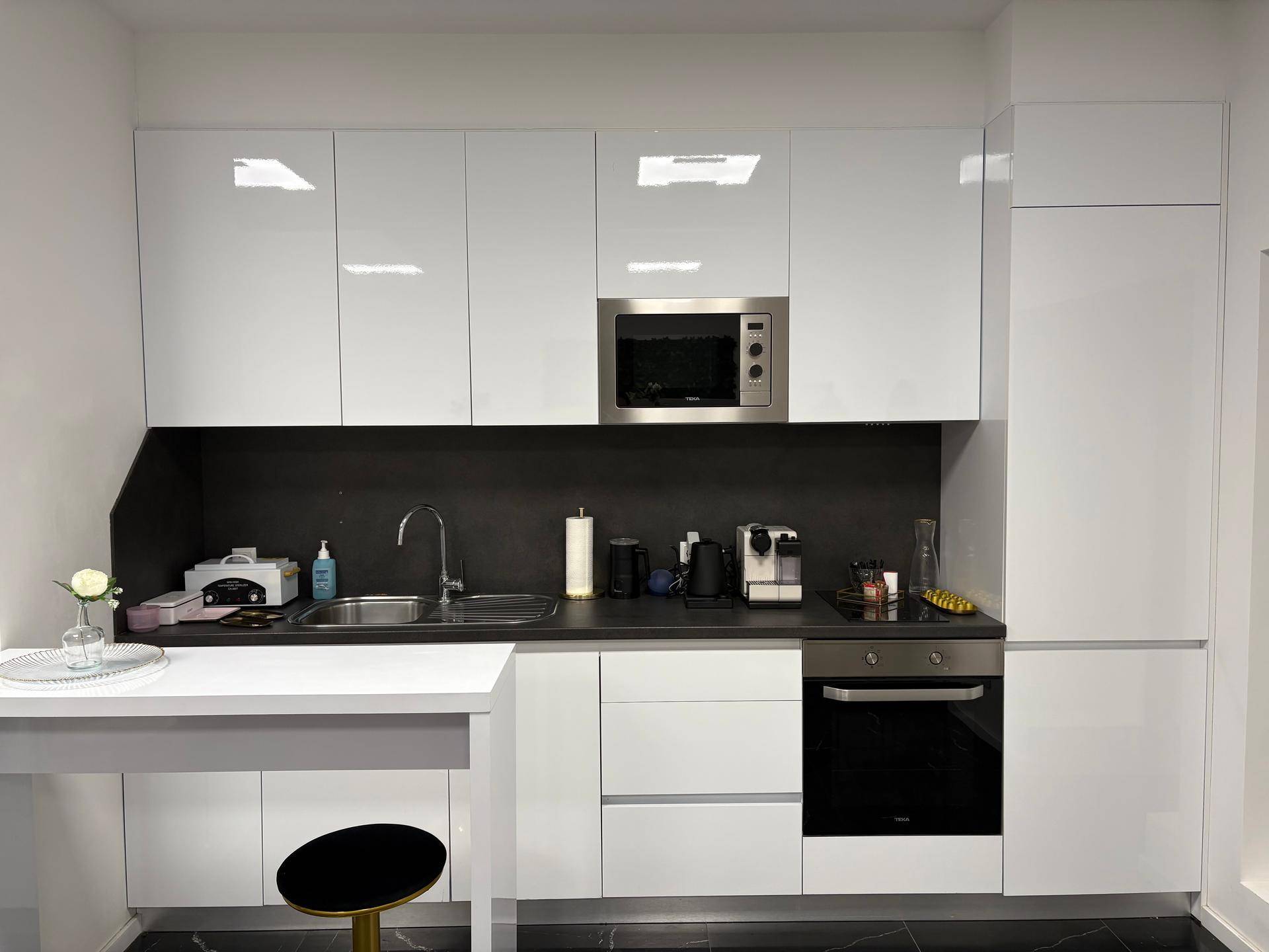 Moderne Küchenzeile mit weißen Hochglanzschränken, integriertem Backofen und Mikrowelle.