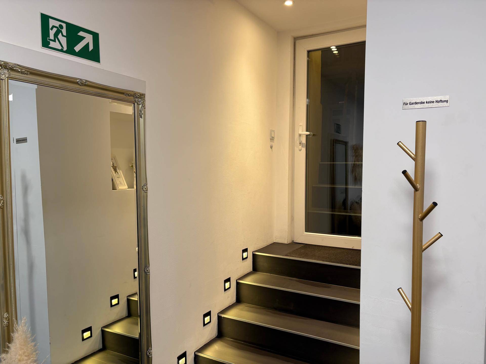 Eingangsbereich mit Treppe, beleuchteten Stufen und großem Spiegel.