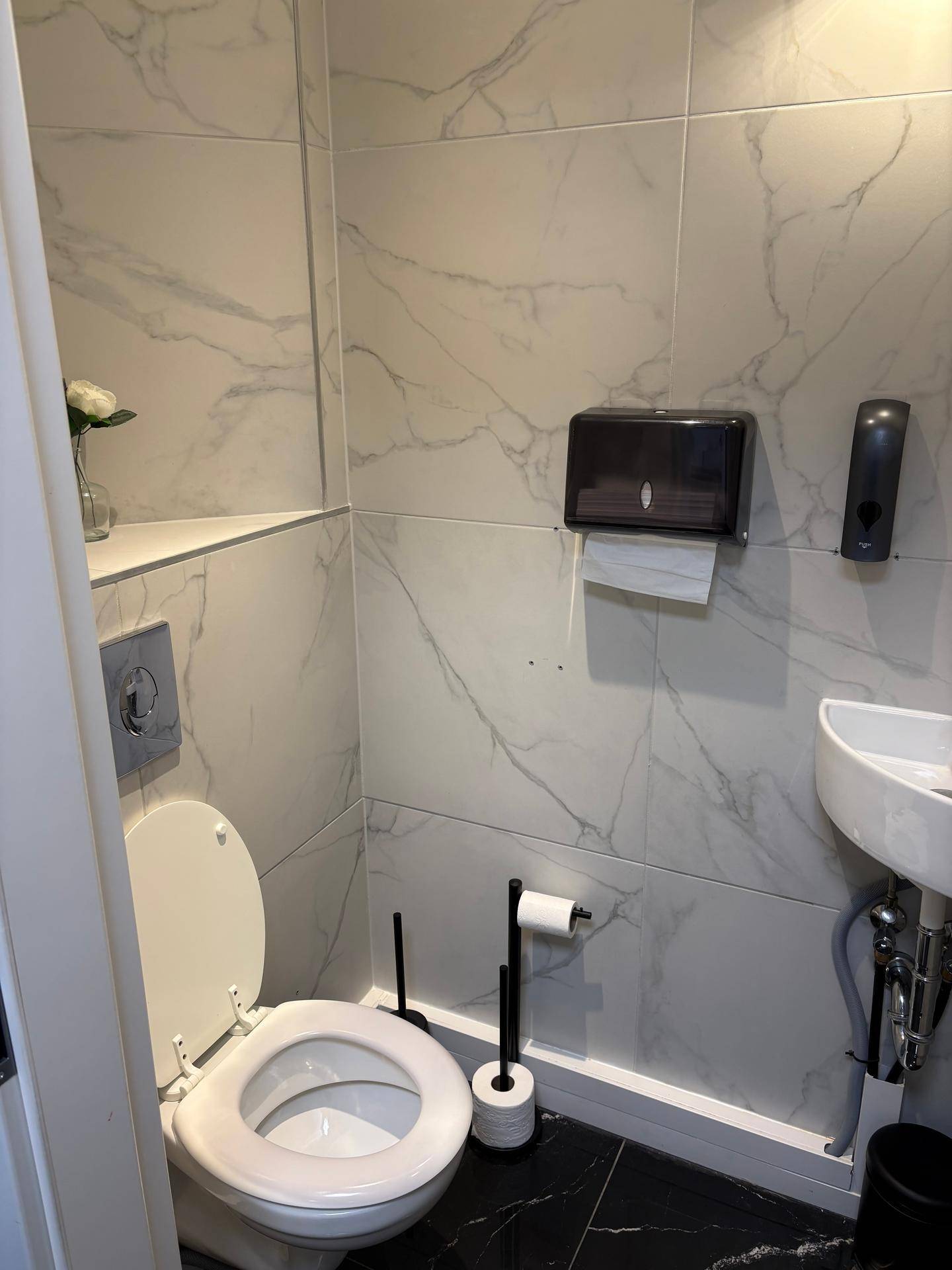 Modernes WC mit Marmoroptik-Fliesen an den Wänden und dunklem Boden.