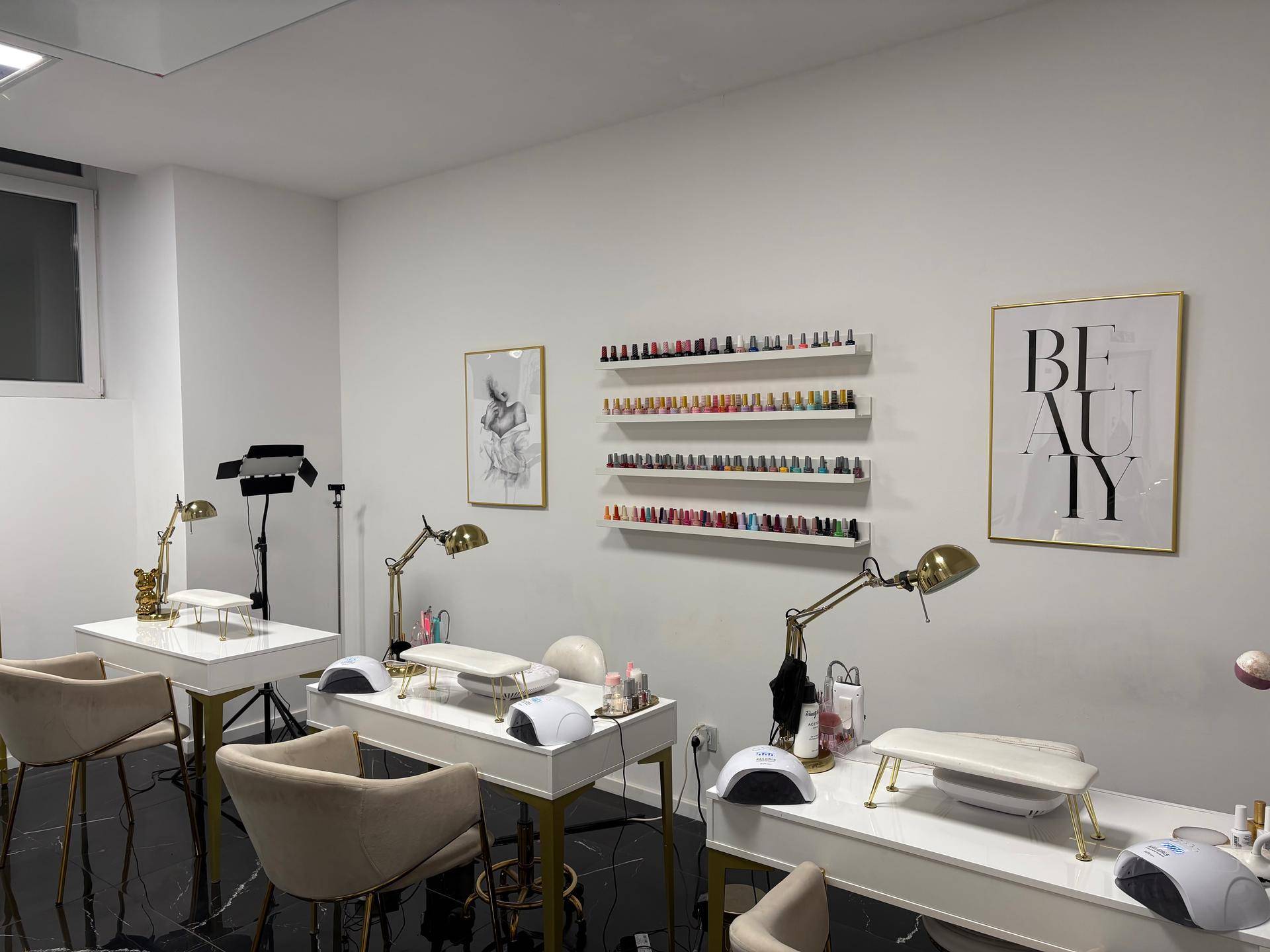 Heller Nagelstudio-Bereich mit mehreren Arbeitsplätzen, Nagellackregalen und modernen Lampen.