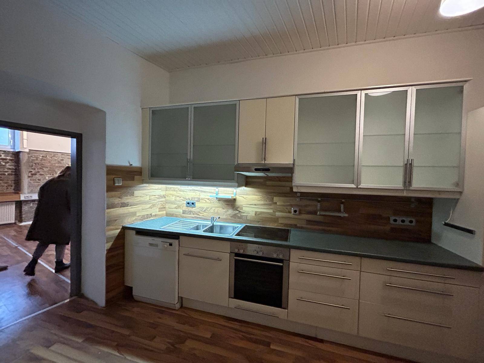 Funktionale Küche mit hellen Fronten, Holzdetails und Blick in einen angrenzenden großen Raum.