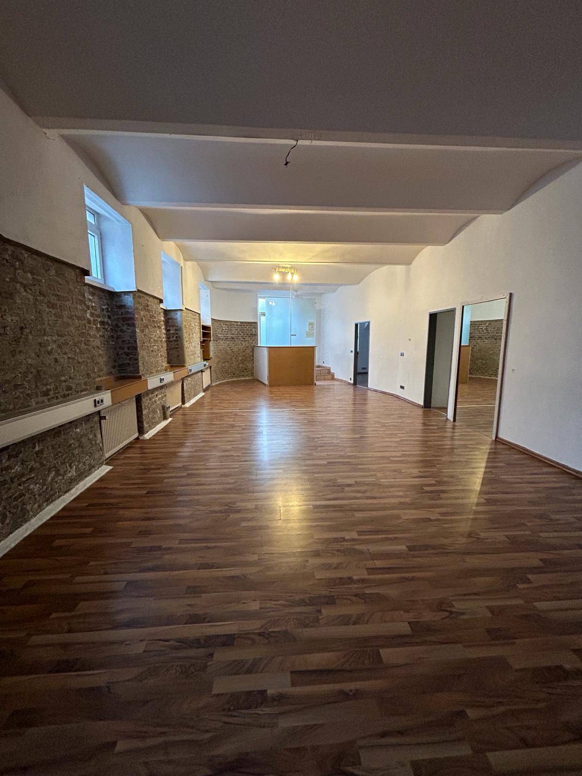 Geräumiger, heller Raum mit Laminatboden und teilweise sichtbaren Steinwänden, ideal für verschiedene Nutzungen.