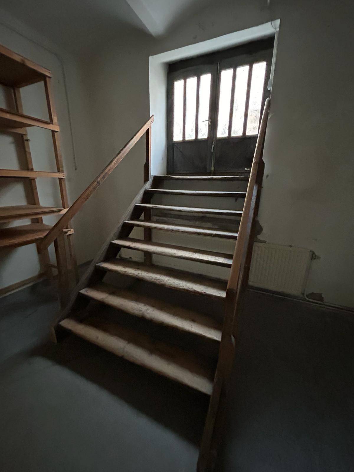 Holztreppe führt zu einer Tür mit Glasfeldern, umgeben von schlichten Wänden und Regalen.