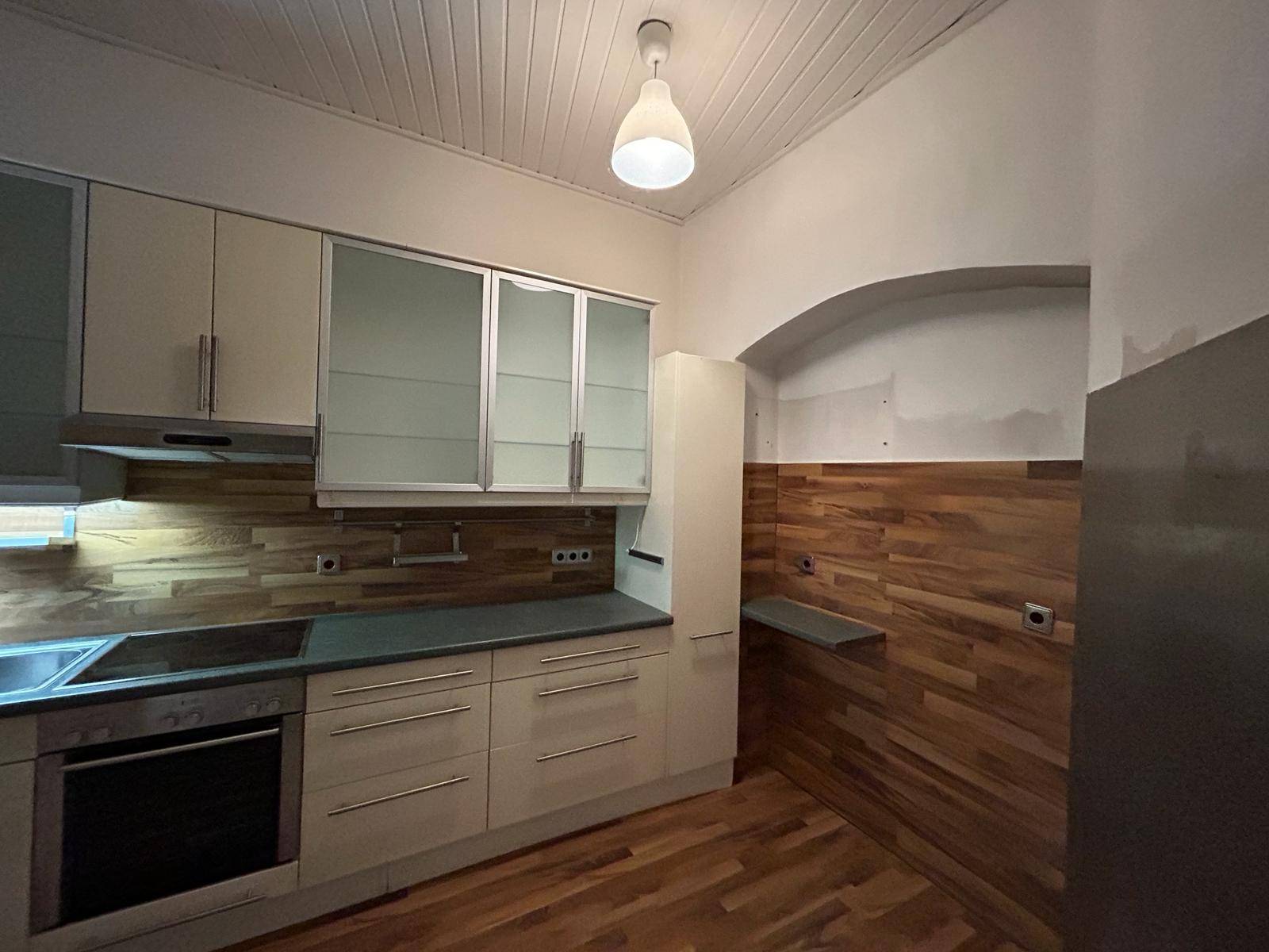 Helle Küche mit beigen Schränken, Holzrückwand und integrierten Geräten, bereit zur Nutzung.