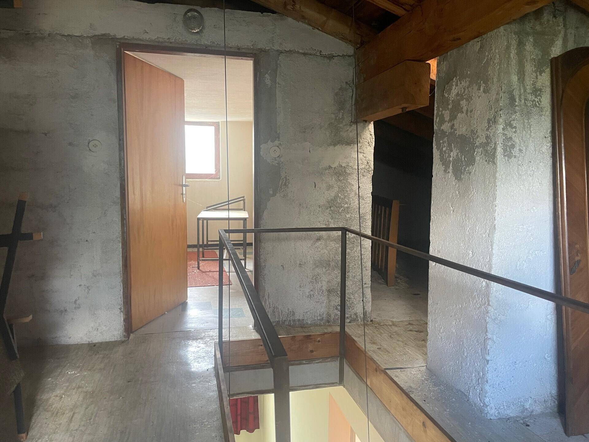 Dachgeschoss mit sichtbaren Holzbalken, Betonwänden und Blick in einen weiteren Raum.
