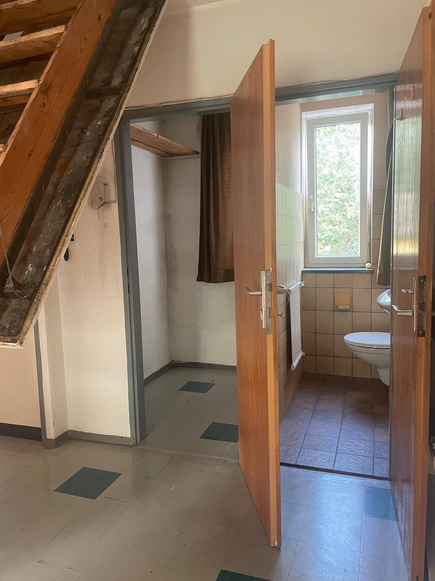 Badezimmer mit beigefarbenen Fliesen, Toilette und Fenster, zugänglich vom Flur.