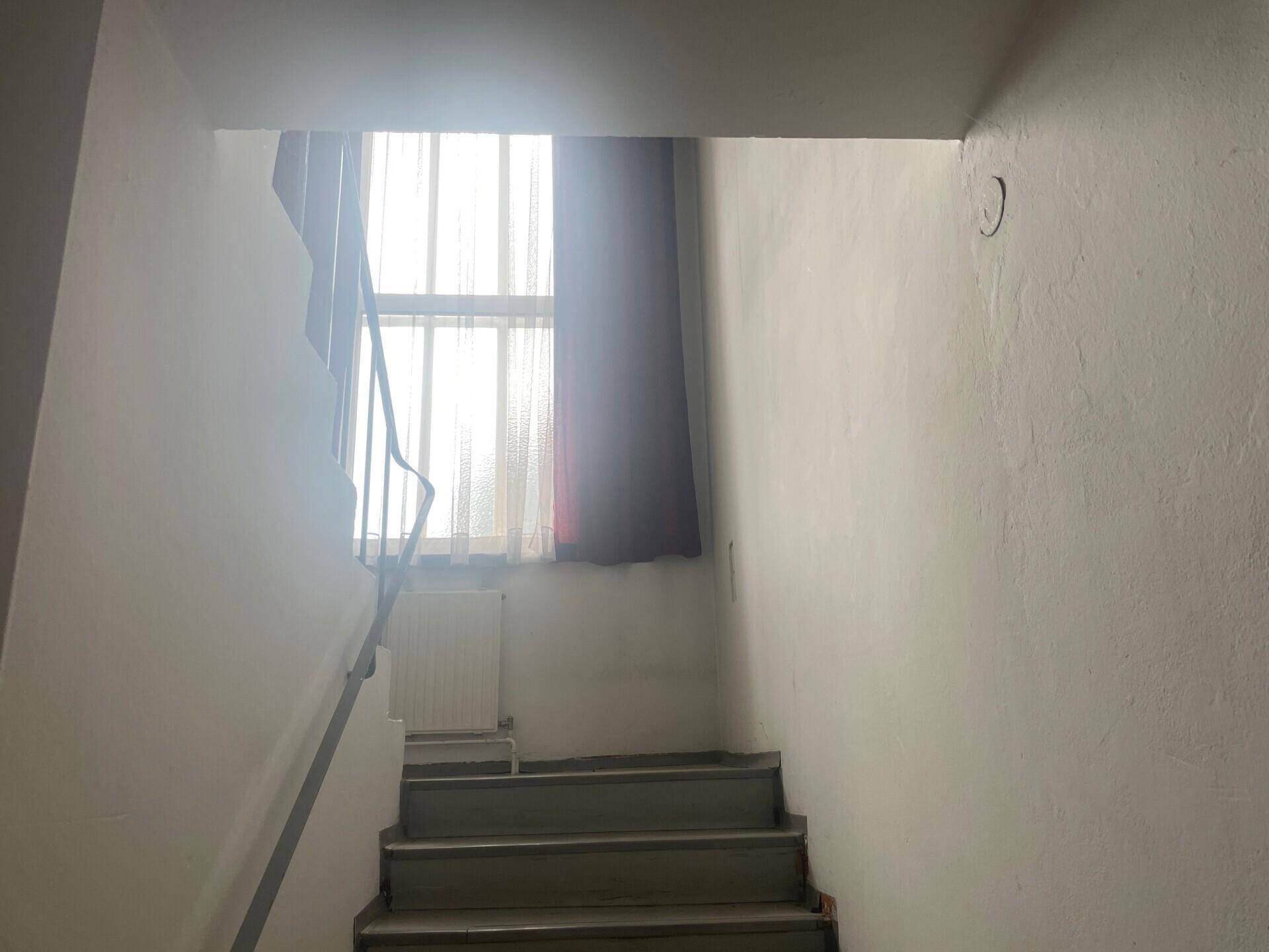 Treppenhaus mit weiß gestrichenen Wänden und einem Fenster mit dunklem Vorhang.