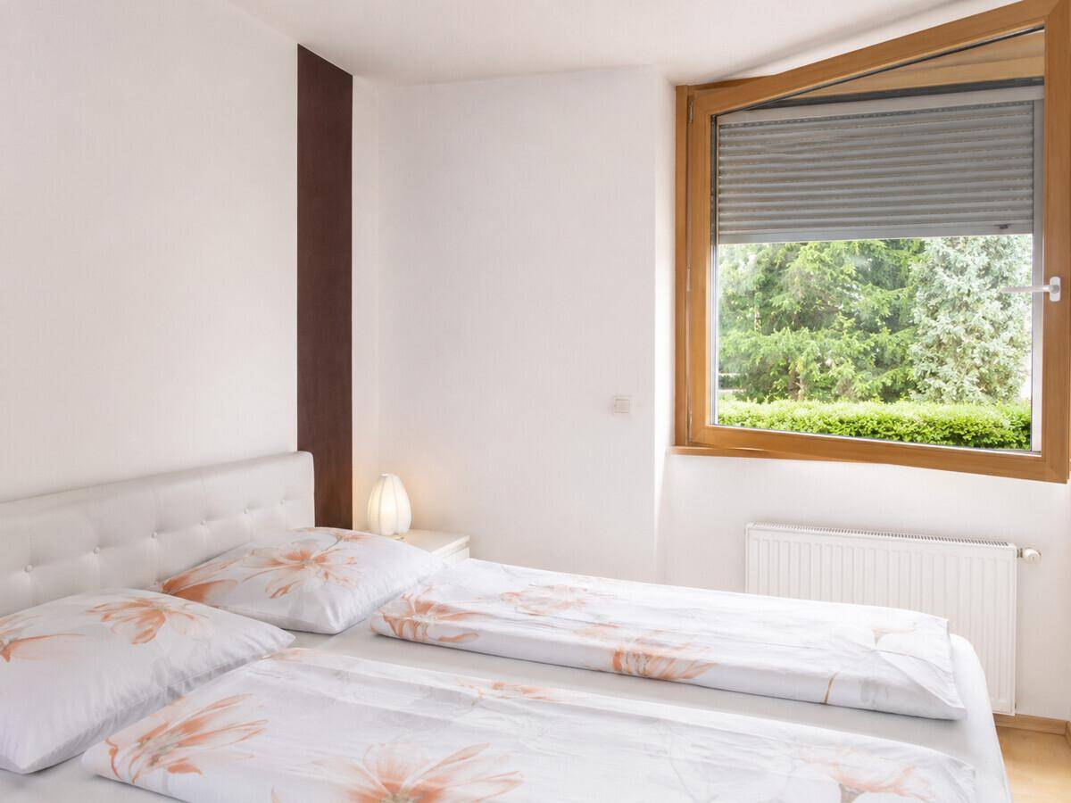 Helles Schlafzimmer mit Doppelbett, Heizung und Fenster mit Blick ins Grüne.