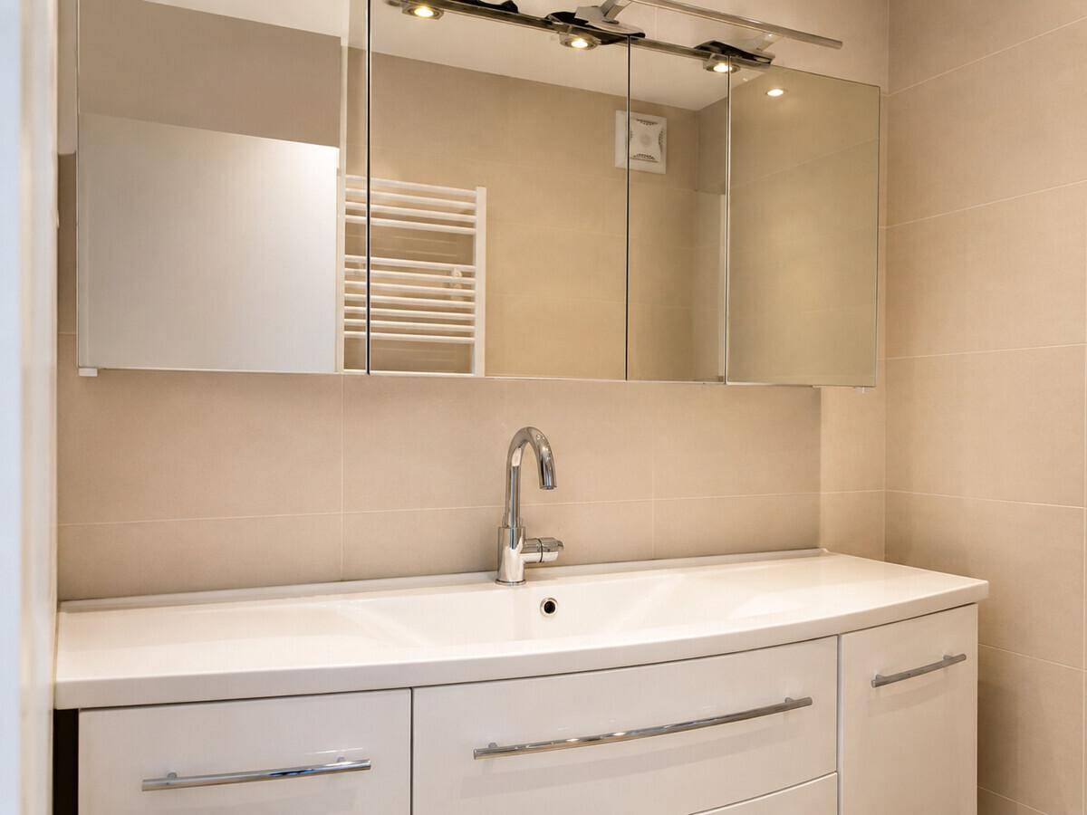 Modernes Badezimmer mit Waschbecken, Spiegelschrank und beigefarbenen Fliesen.