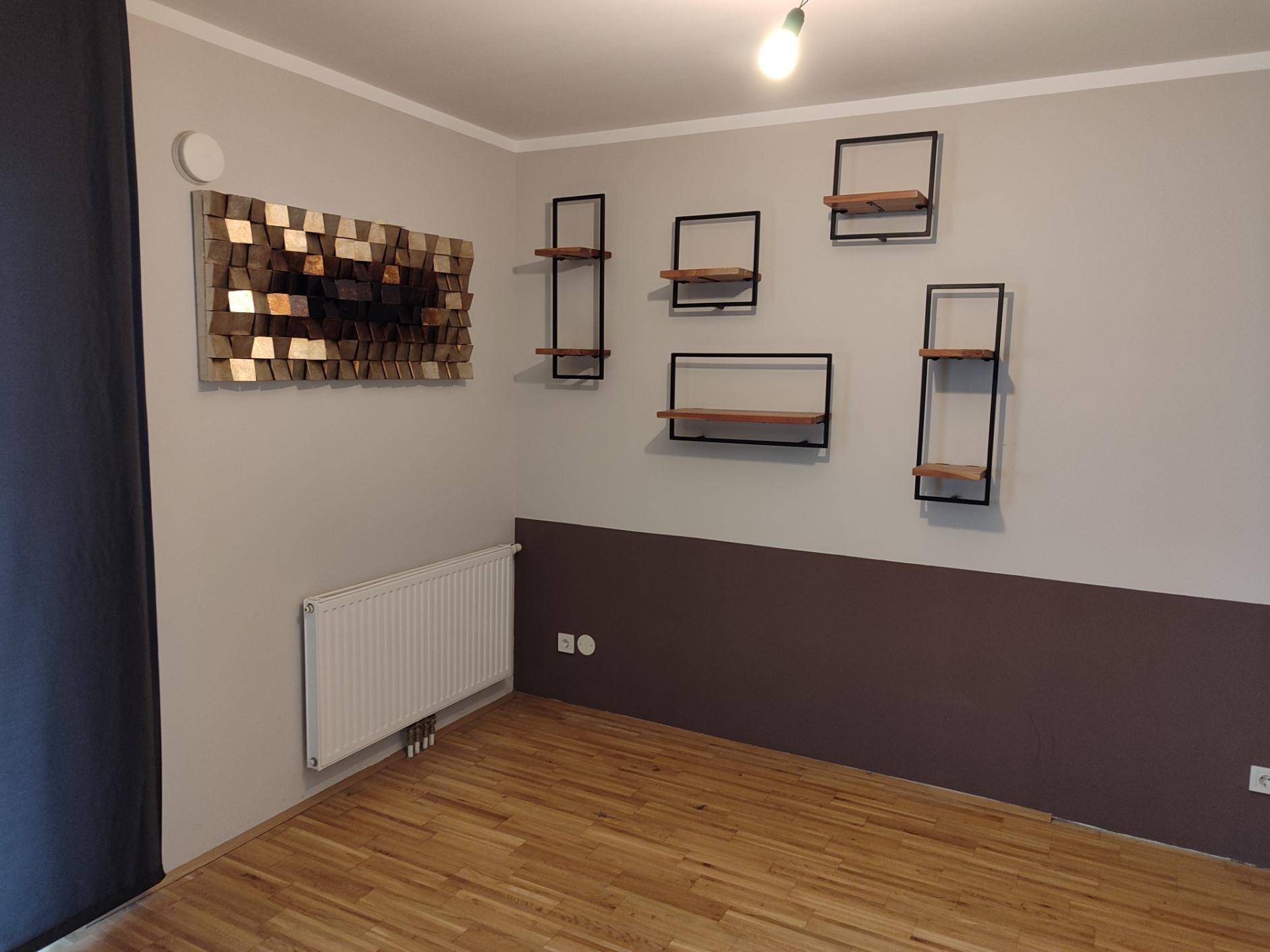 Wohnzimmerwand mit dekorativen Regalen und einem Heizkörper.